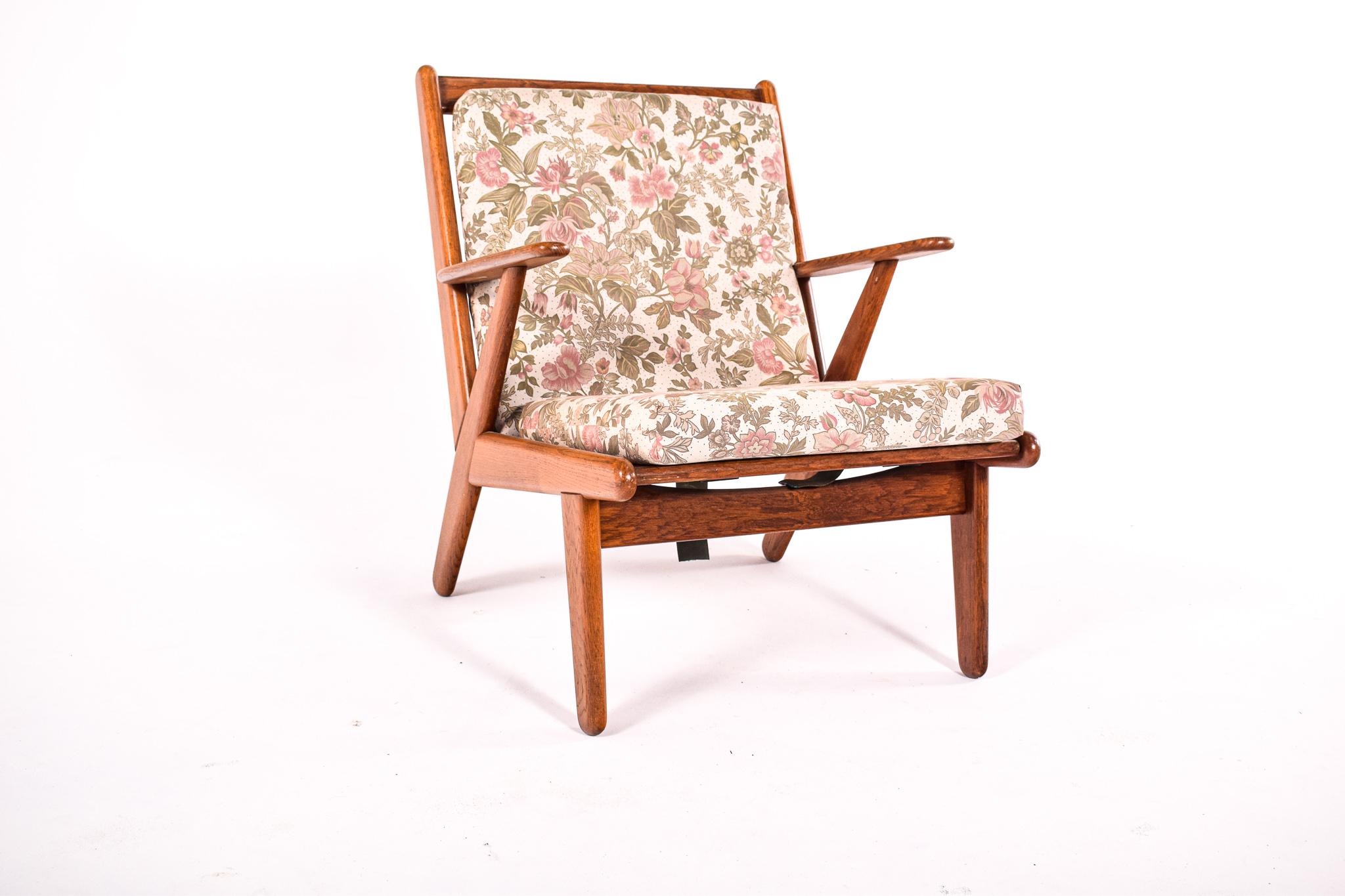 This easy chair, a piece of mid-century design from the 1950s, is crafted from oak, a wood renowned for its strength and durability. The chair's design is quintessentially of its era, featuring a slatted back that provides both support and a