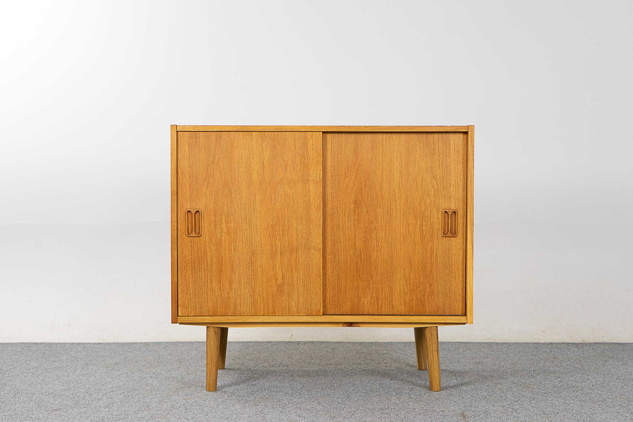 Oak Danish cabinet, circa 1960's. Solid wood handles, adjustable shelf and removable legs. Compact design, the perfect condo sized storage solution.