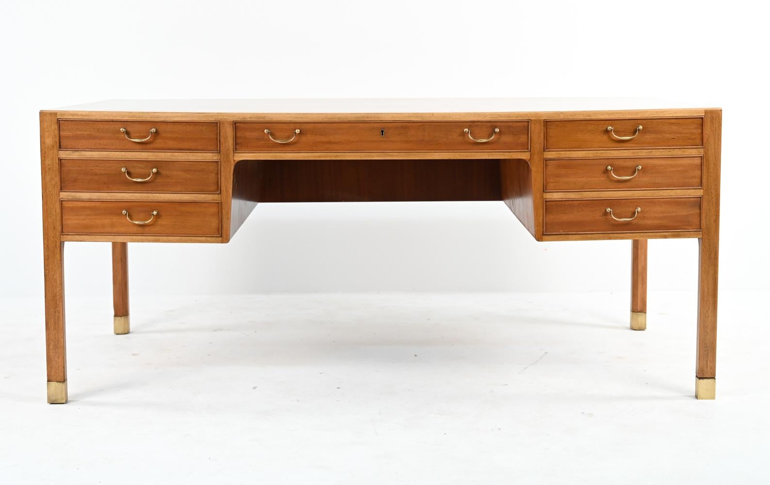 A handsome Danish mid-century executive desk designed by Ole Wanscher for AJ Iversen in generous proportions. This large desk features one central drawer flanked by three drawers on either side, all sporting traditional brass bale handles to