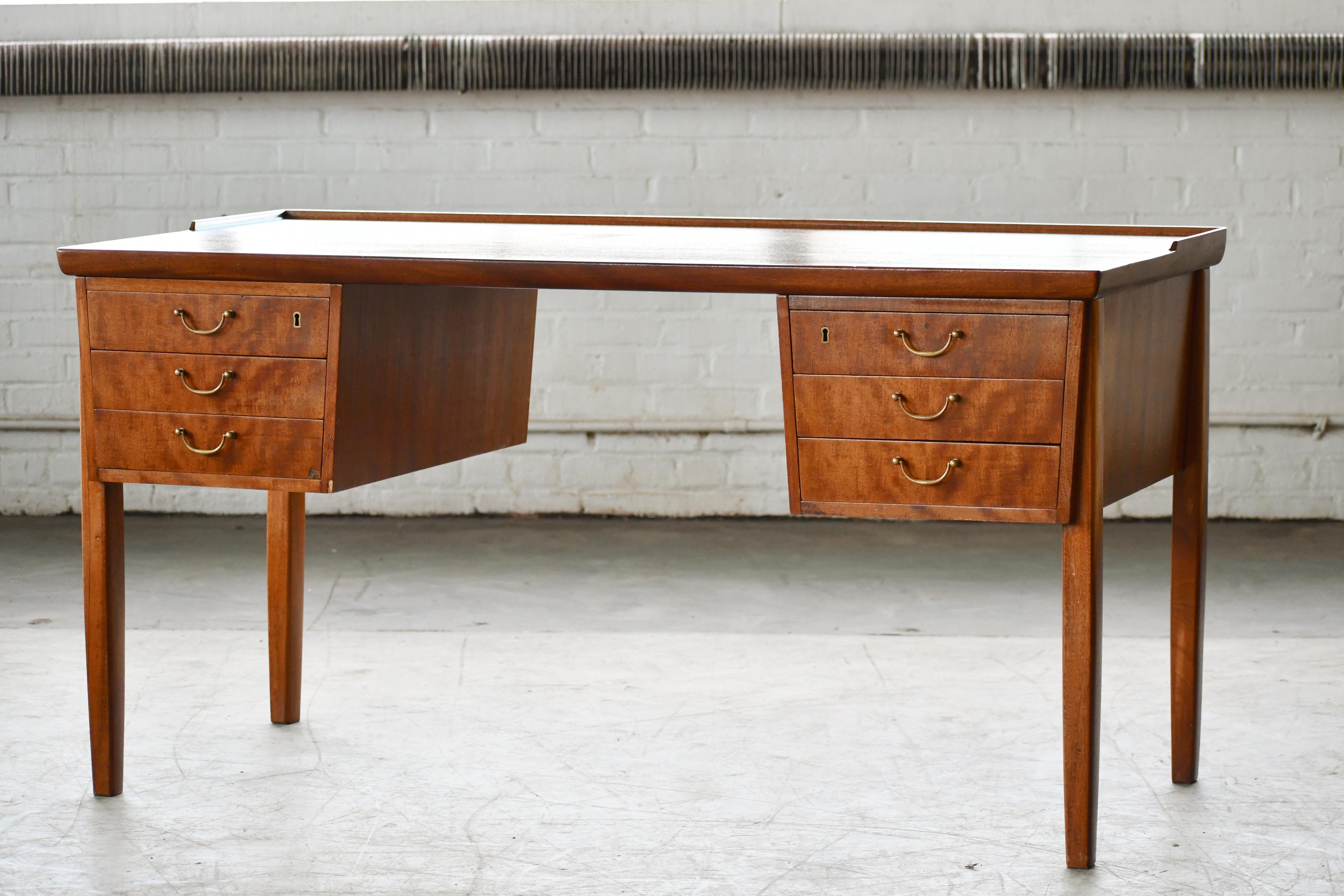 Danish Mid-Century Ole Wanscher style writing desk in mahogany ca. 1950. Elegant very functional table. The brass pulls are typical for the era we love the shape of the tapered legs which are less typical and provide for a nice modern look. Nice
