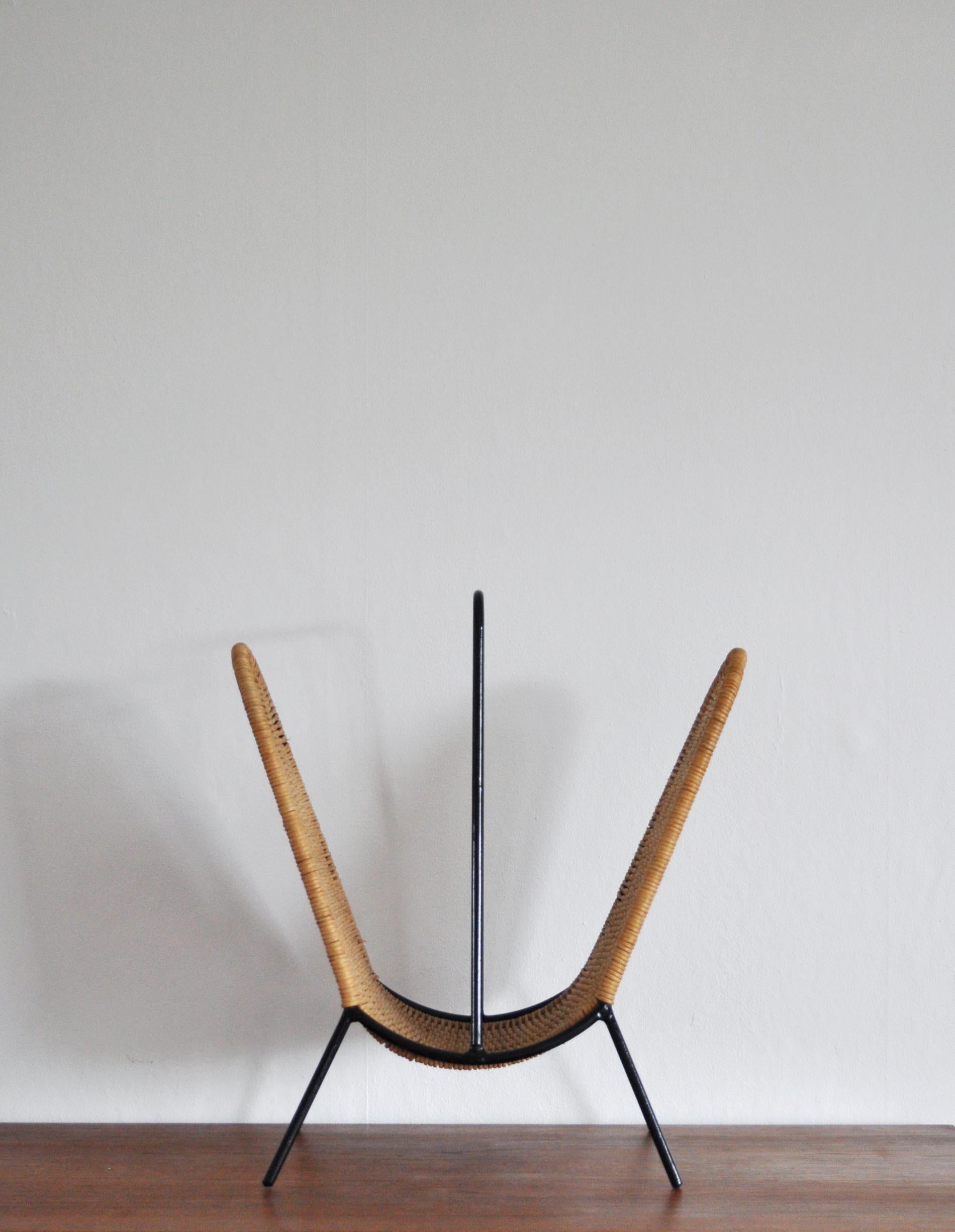 Danish Magazine stand or rack circa 1960s, features woven rattan strands which wrap around the black painted steel wire frame. 
Beautiful minimalistic Scandinavian Modern design attributed to Carl Auböck. Performed for Illums Bolighus.
Suitable for