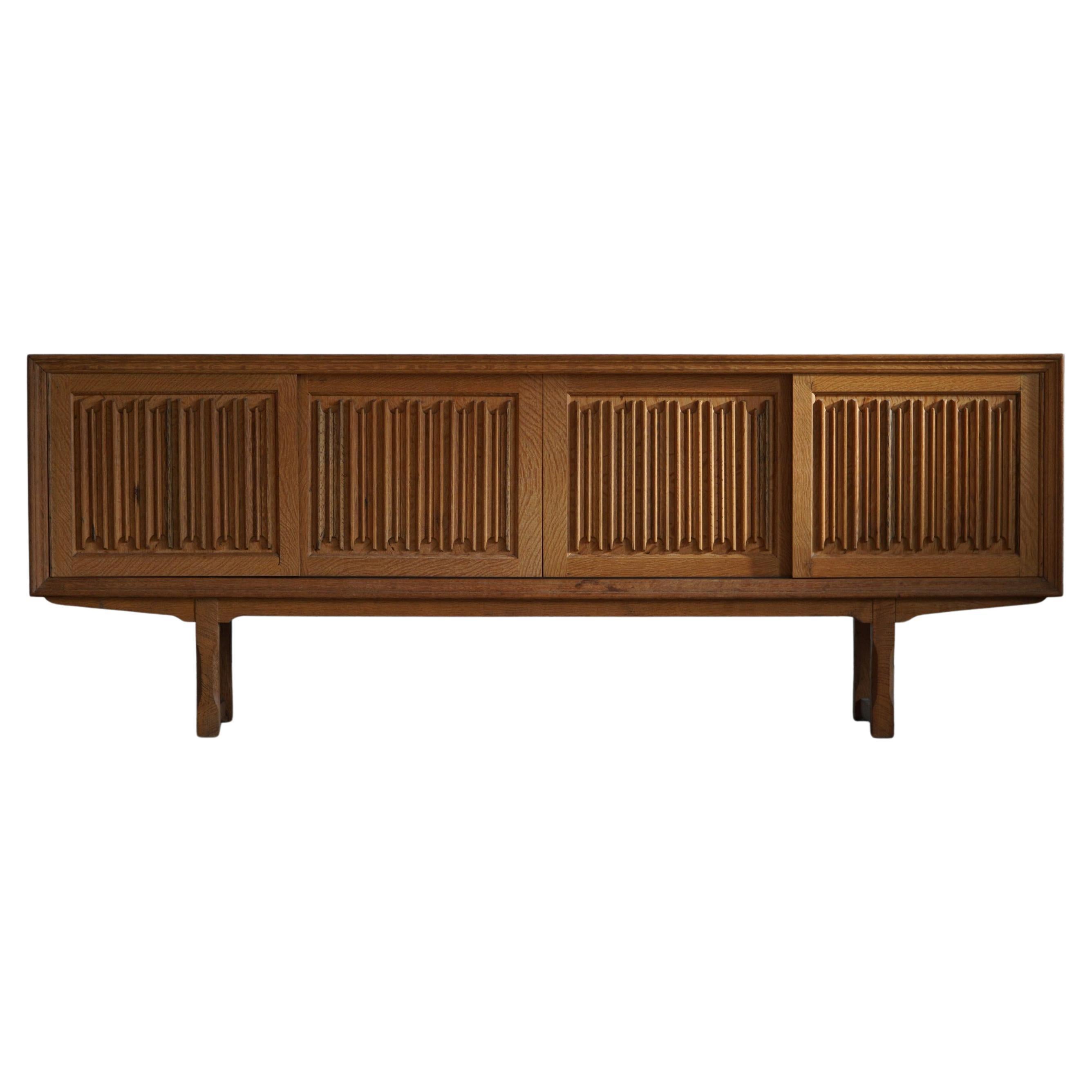 Low modern sideboard, made in oak. Crafted by a Danish cabinetmaker, ca 1950s.
Four sliding doors, inside storage and drawers.

A great patina and a nice sculptural front design. 

With a heavy focus on functionality, this design style leans
