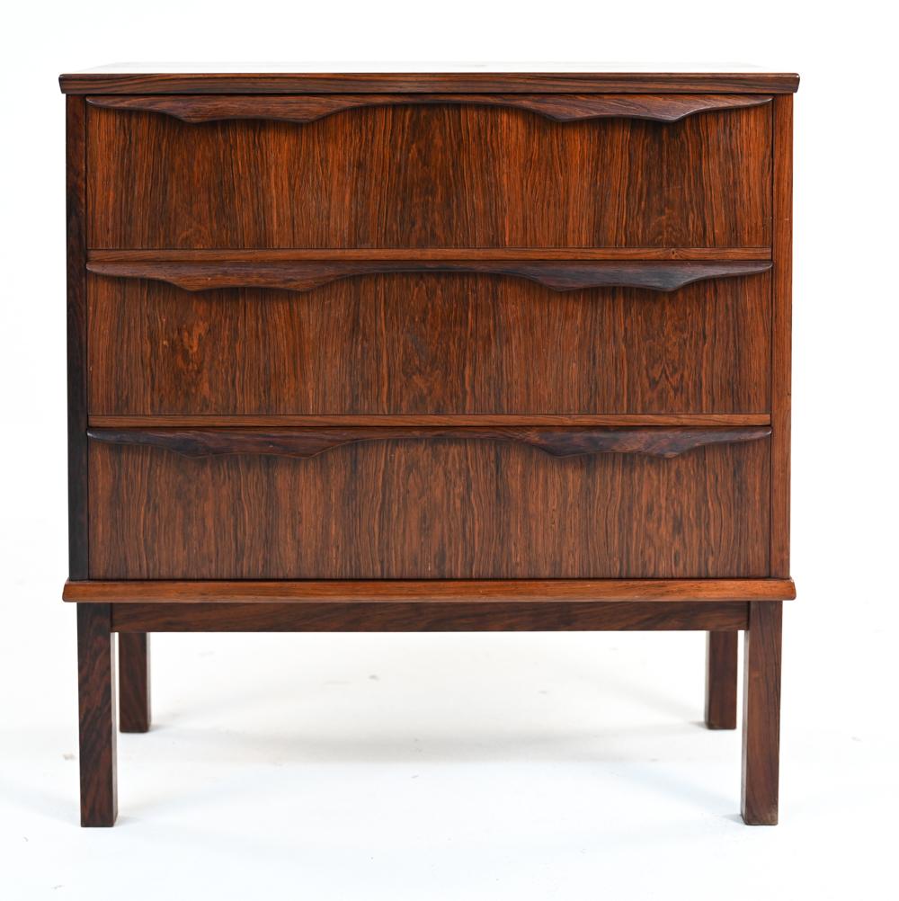 A handsome Danish mid-century petite chest of drawers in rosewood with shaped drawer pulls. Diminutive proportions lend this chest to be the perfect nightstand or accent piece in an apartment. No apparent labels.