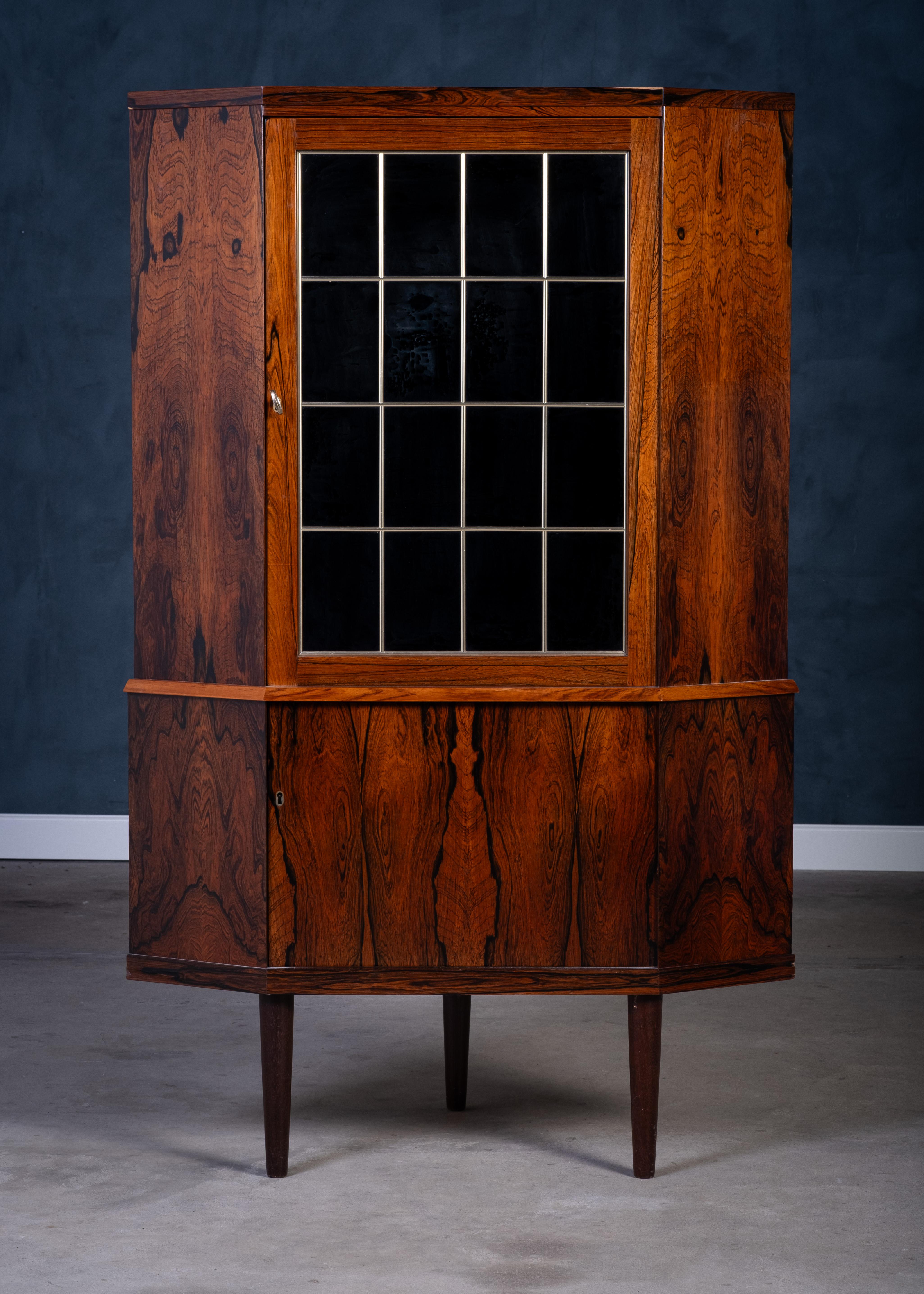 Elegante mobile angolare danese degli anni '60 realizzato in legno di palissandro dalla ricca venatura. Presenta un bellissimo vetro scuro piombato e un generoso spazio di archiviazione all'interno. Un pezzo elegante e funzionale che aggiunge calore