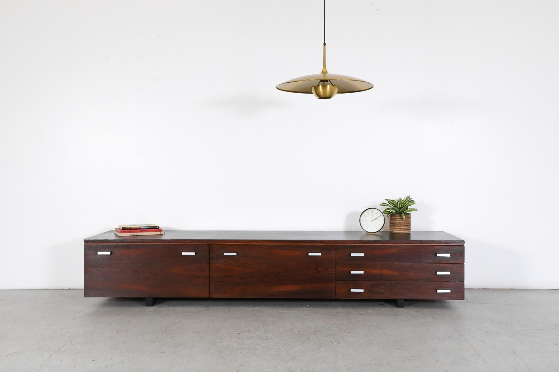 Mid-Century rosewood credenza with black lacquered top and complimenting brushed aluminum drawer pulls. This low credenza has three felt lined drawers next to double drop down storage cabinets with birch interiors. Frame is lightly refinished with