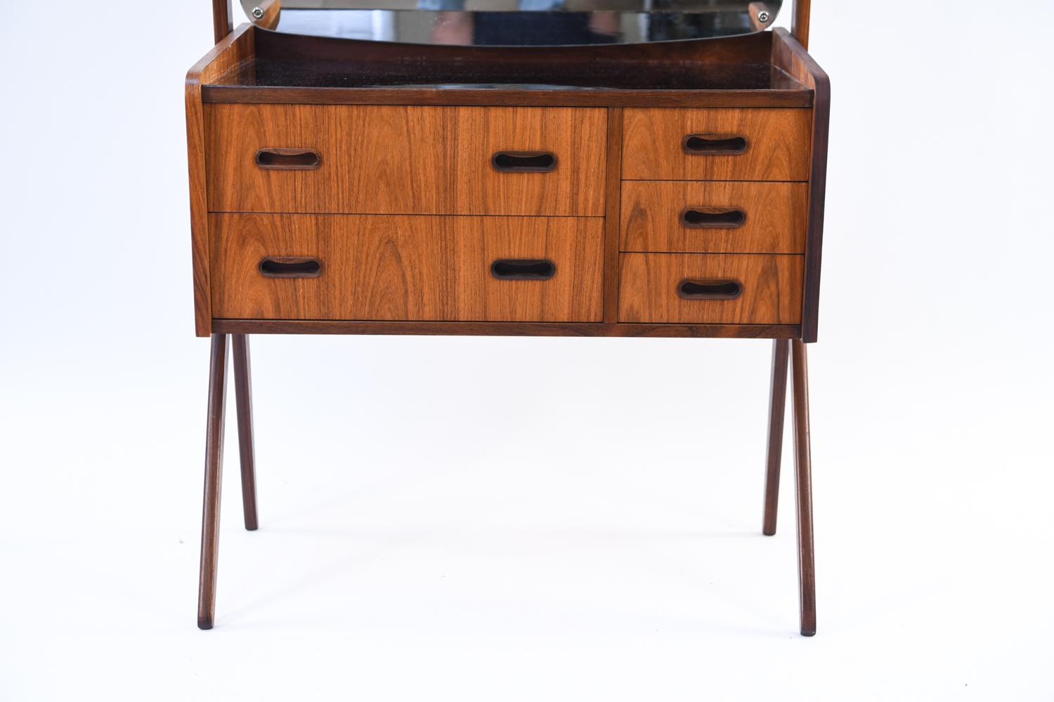 This Danish midcentury rosewood vanity has a mirrored back with rounded corners, upon a slender frame with angled legs. Drawers for storage make up the central portion of this modern piece.