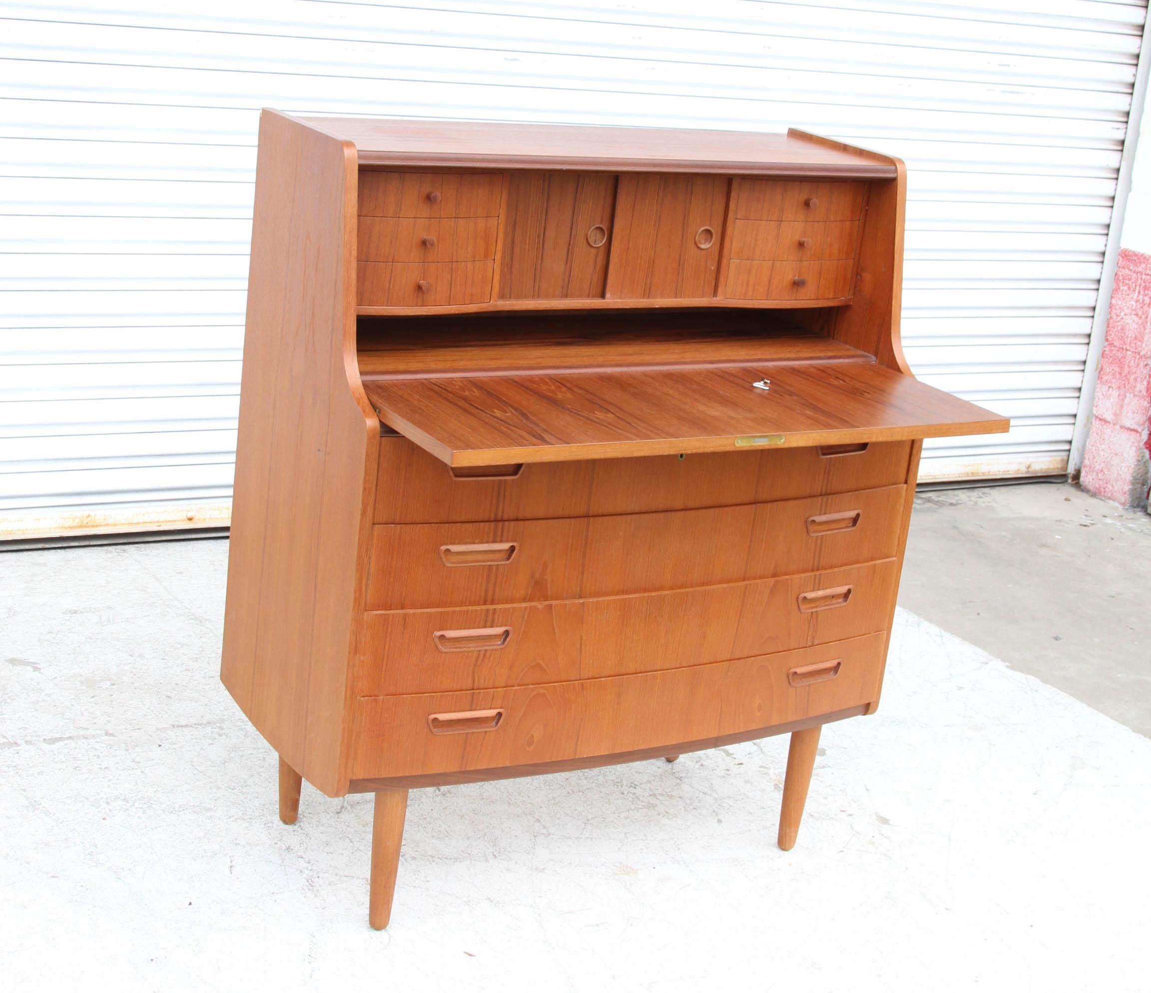 Vintage Danish midcentury teak secretary desk.
 
Danish modern teak secretary desk features a lockable, pull-down work surface opening to 6 drawers and sliding storage. One key is present. 
Pulls are reminiscent of Arne Vodder. Four tapered legs.