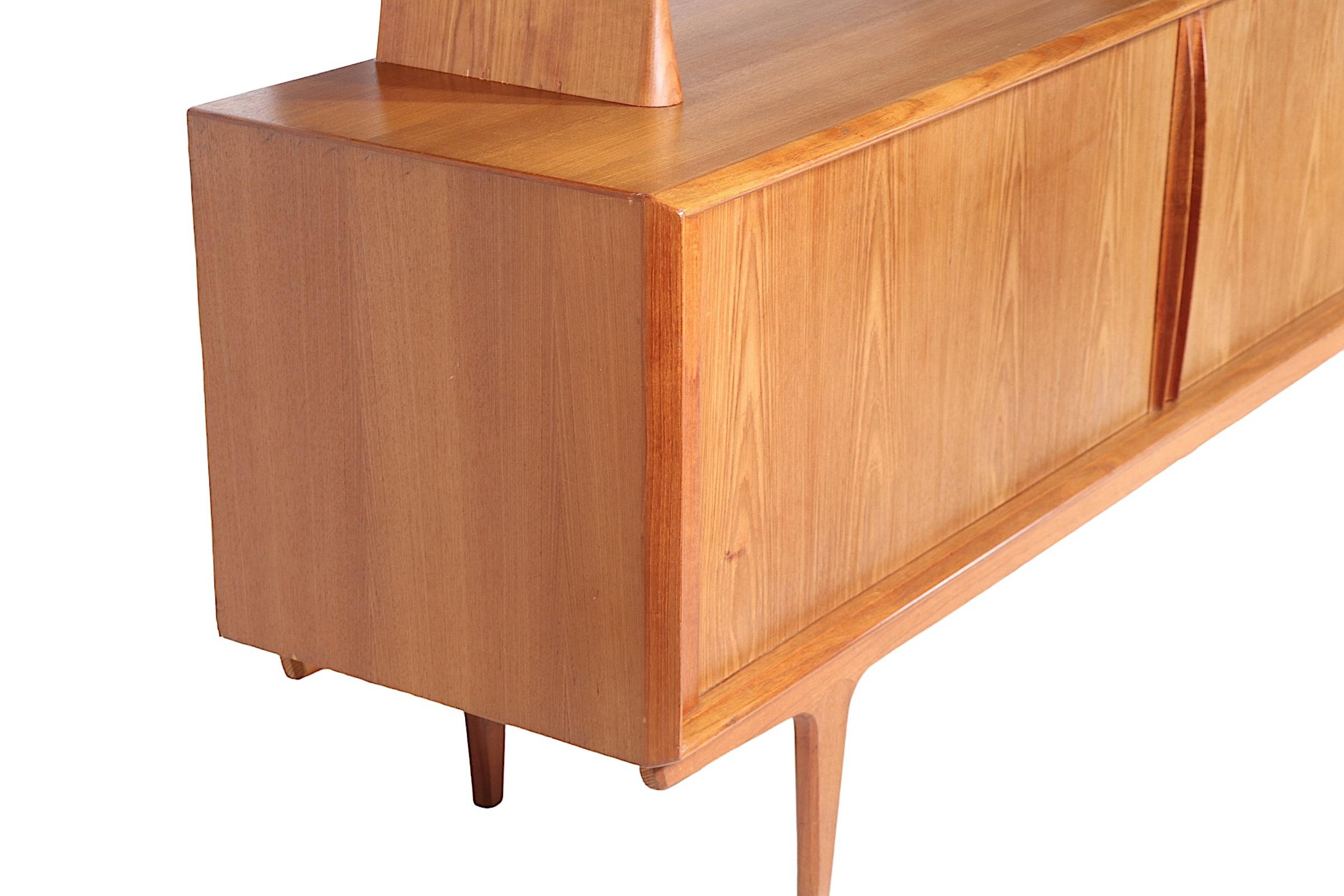Exceptional Danish Mid Century Modern showcase sideboard, credenza, made in Denmark by Bernard Pedersen & Son, circa 1960's. The lowercase features two sliding tambour door, which open to a center bank of four drawers, flanked by open shelved