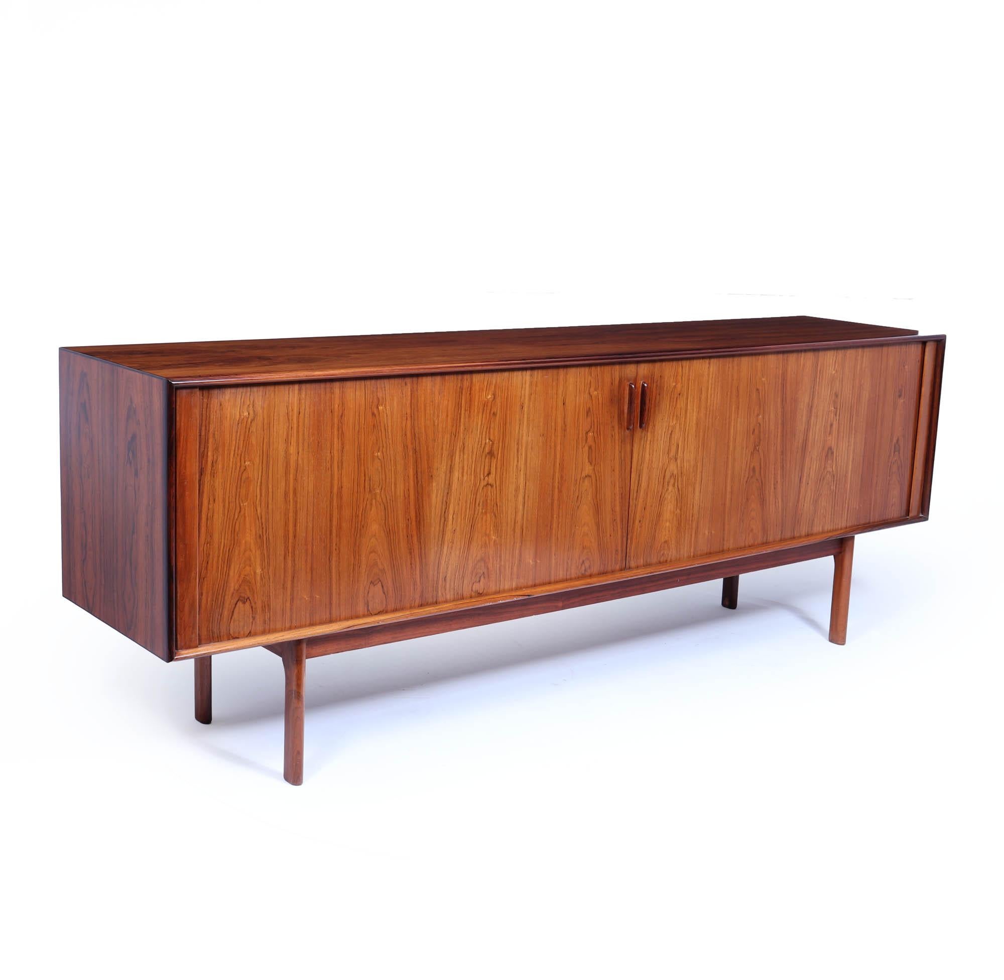 A mid-century Danish sideboard, designed by Bernhard Pedersen in the 1960s. This remarkable item has tambour doors that slide effortlessly, creating a seamless look with the cabinet's interior. Inside, you will find adjustable shelves and four