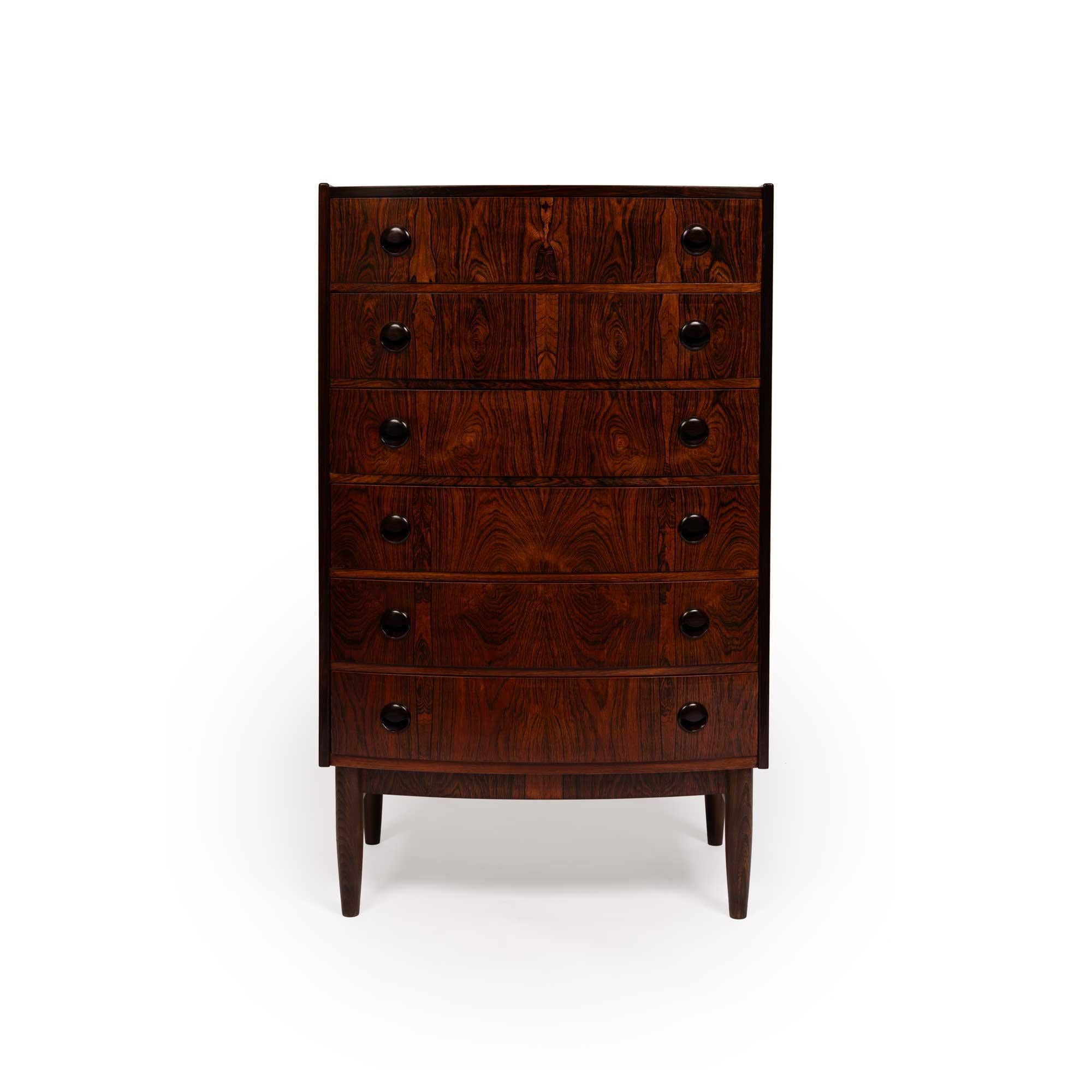 This exquisite rosewood tallboy dresser, crafted in Denmark during the 1960s, epitomizes the superior craftsmanship of the Danish mid-century modern movement. Its elegant bow-front design features six smoothly operating drawers, each adorned with