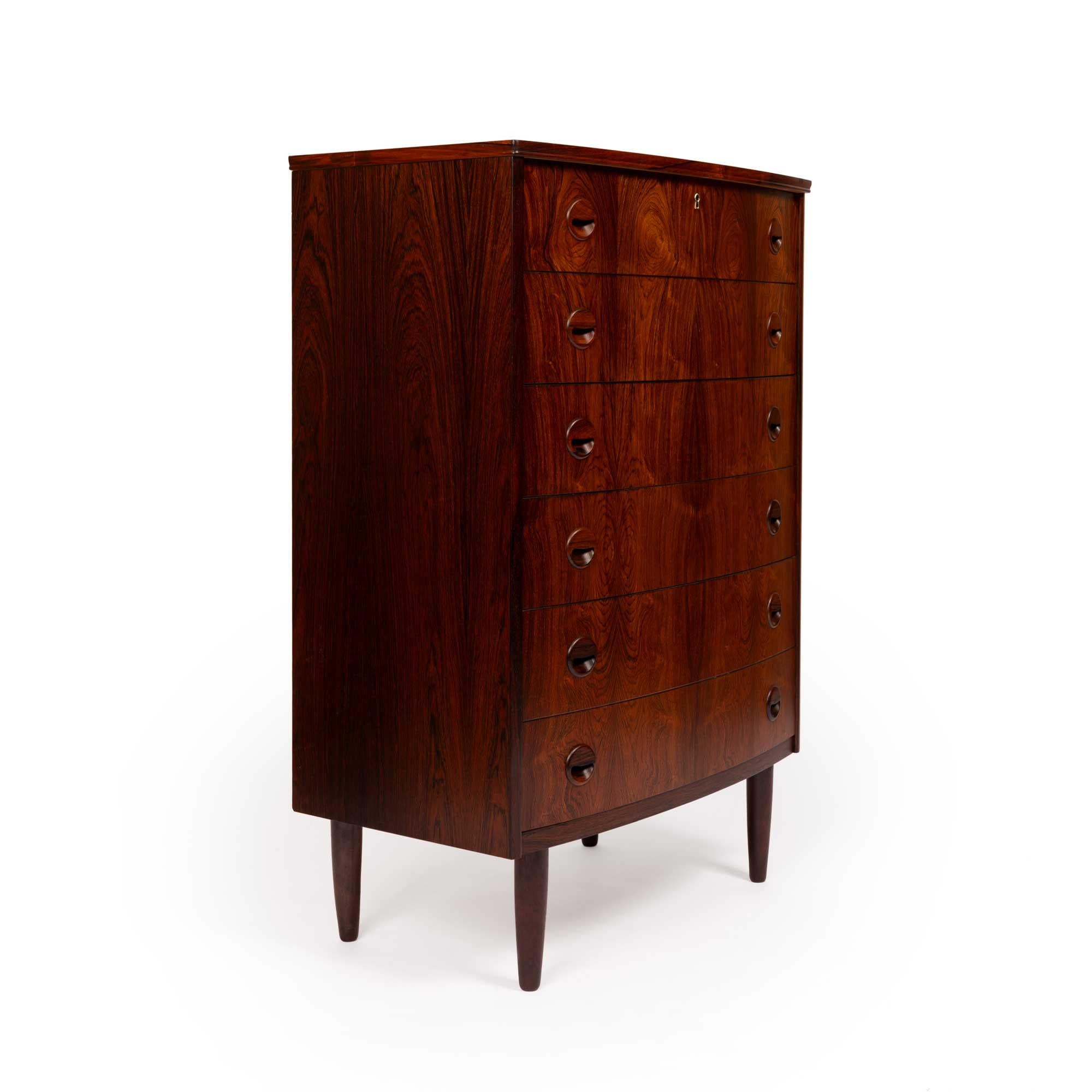 This exquisite rosewood tallboy dresser, crafted in Denmark during the 1960s, epitomizes the superior craftsmanship of the Danish mid-century modern movement. Its elegant bow-front design features six smoothly operating drawers, each adorned with