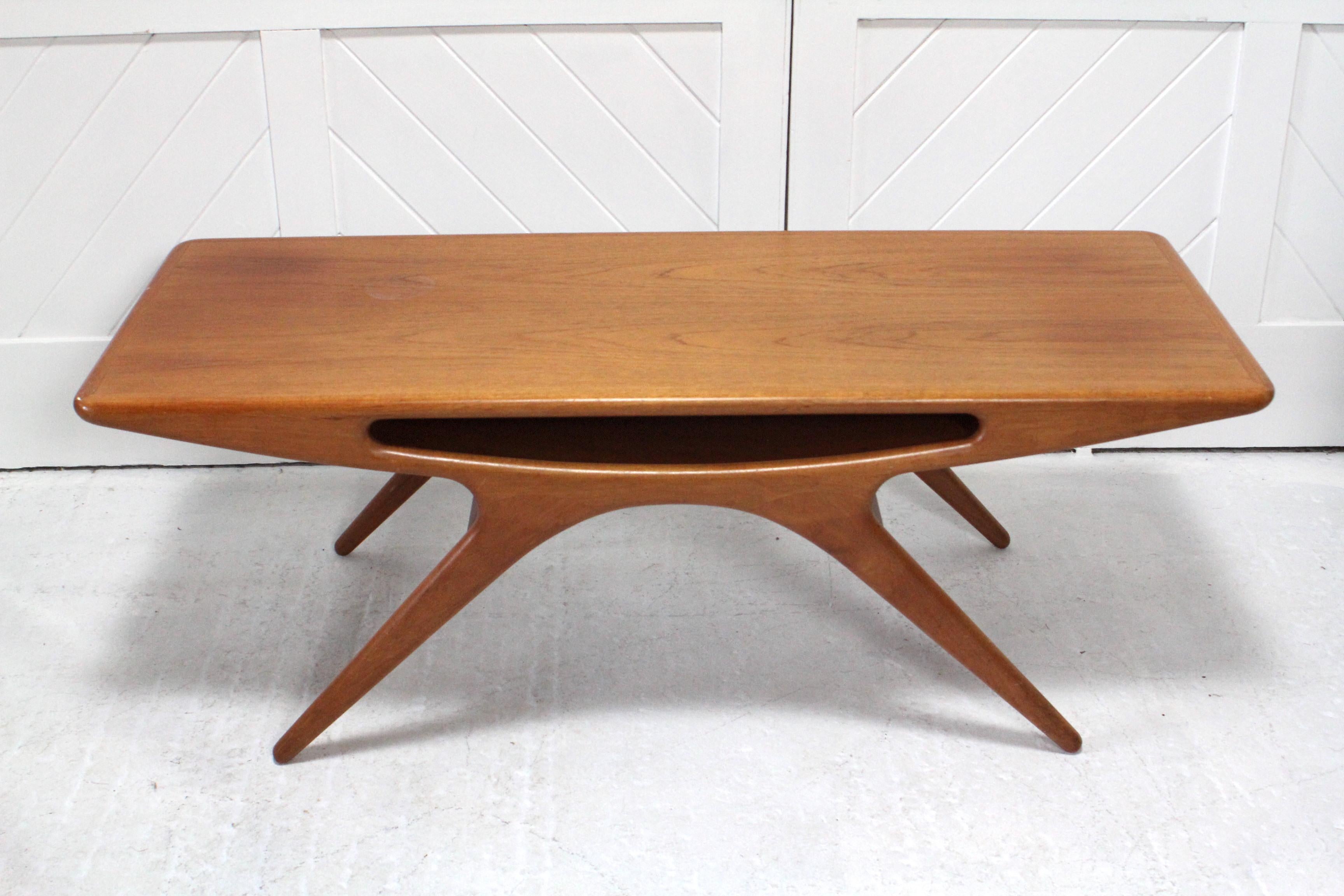 Fifties teak ‘smile’ table with centre pocket shelf.
Johannes Andersen (1903-1991) 
For CFC Silkeborg
Denmark

Johannes Andersen trained as a cabinet maker and opened his own architectural and furniture workshops in the 1930s. The iconic