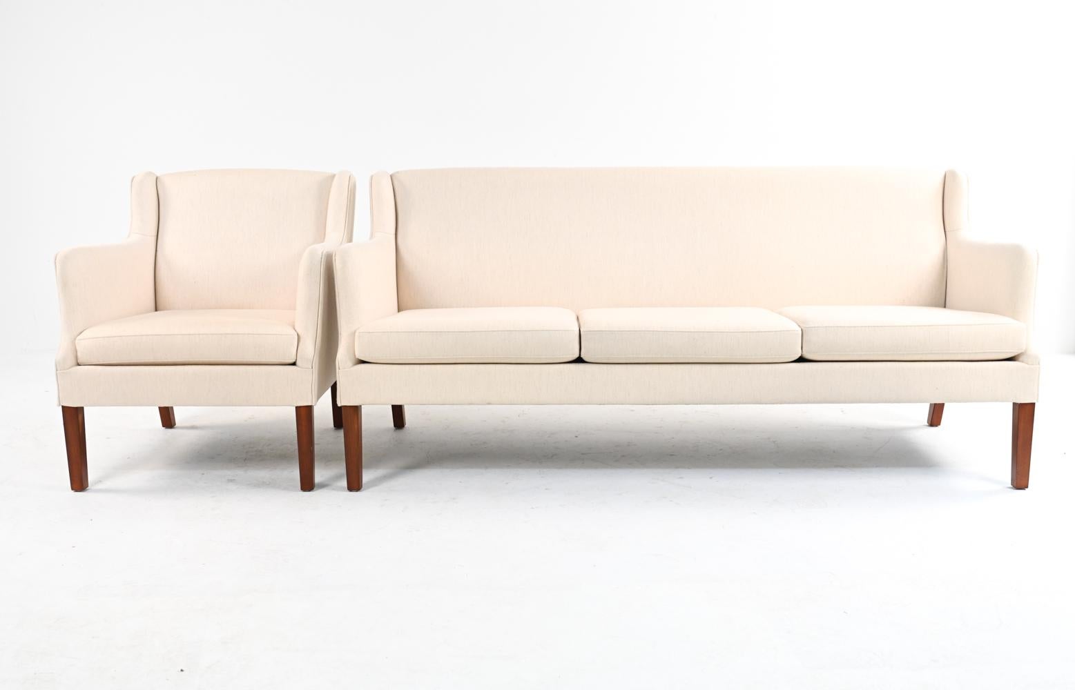 A beautiful three-seater sofa and armchair attributed to Frits Henningsen, c. 1940's-1950's; with later cream wool twill upholstery.
