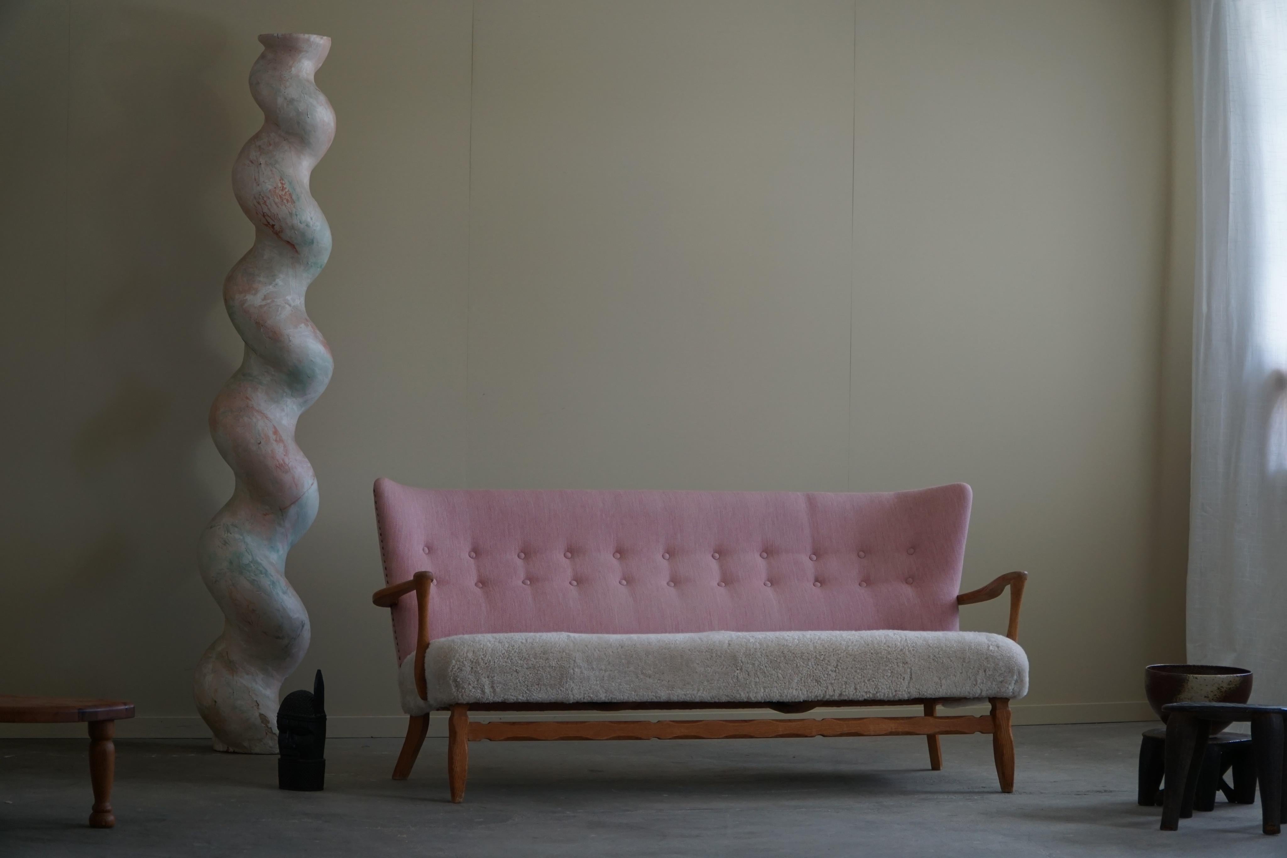 A fine example of a Danish modern sofa in solid oak, reupholstered seats in great quality shearling lambswool, the backrest upholstered in a original pink fabric. Made in the manner of Danish Architect Viggo Boesen in the 1960s. This exquisite sofa