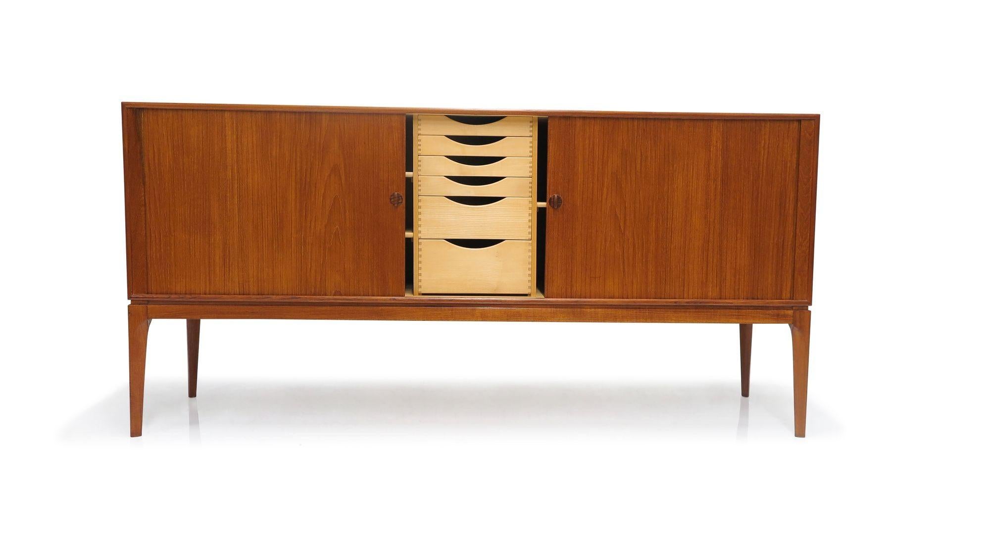 Scandinavian teak credenza, crafted in 1955 in Denmark. This finely crafted cabinet, made of teak with mitered corners, features tambour doors with sculpted pulls. The doors open to reveal a birch interior with adjustable shelves and silverware
