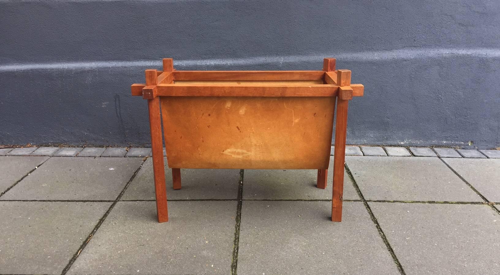 Magazine rack in teak and patinated leather made by Skjode Skjern, Denmark in the 1950s. The design is simplistic, yet the construction shows distinct wooden joints. A thick leather cradle hangs in the wooden frame and provides plenty of storage
