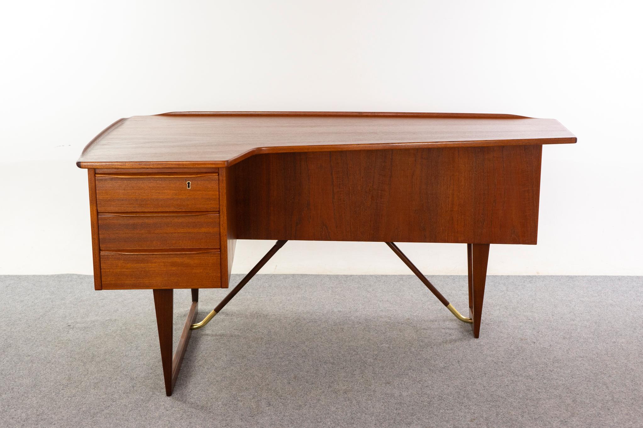 Teak Danish boomerang desk by Peter Lovig Nielsen, circa 1960's. Iconic, eye-catching asymmetrical design with gleaming brass accents. Pencil lip edging, bank of drawers with locking top, rear open bookcase and drop-down lockable bar with original