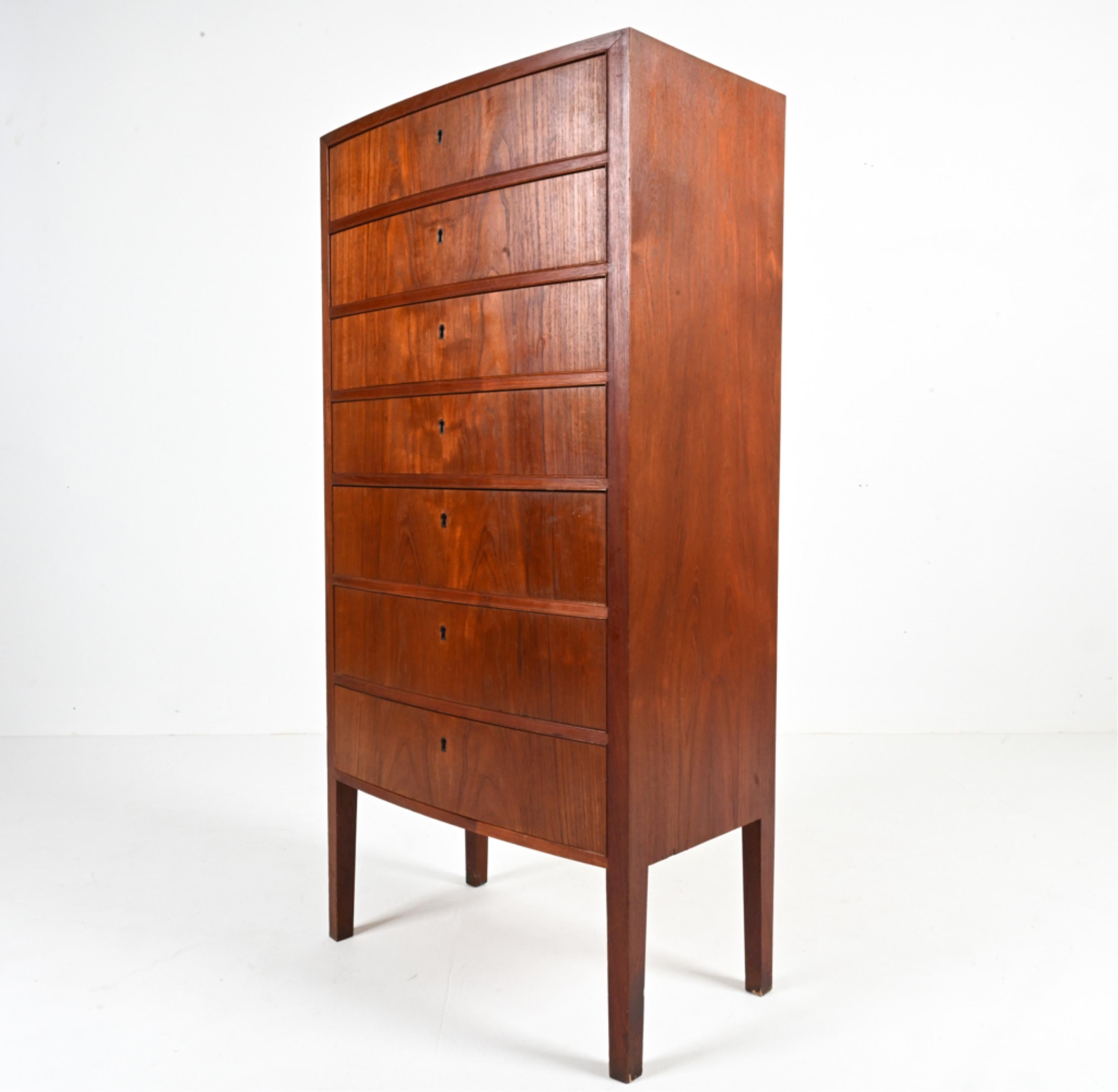 Introducing an exquisite piece of Mid-Century design: a teak bow-front tallboy chest of drawers attributed to the masterful Ole Wanscher, crafted in Denmark around 1950-1960. This iconic chest epitomizes the timeless elegance of Scandinavian