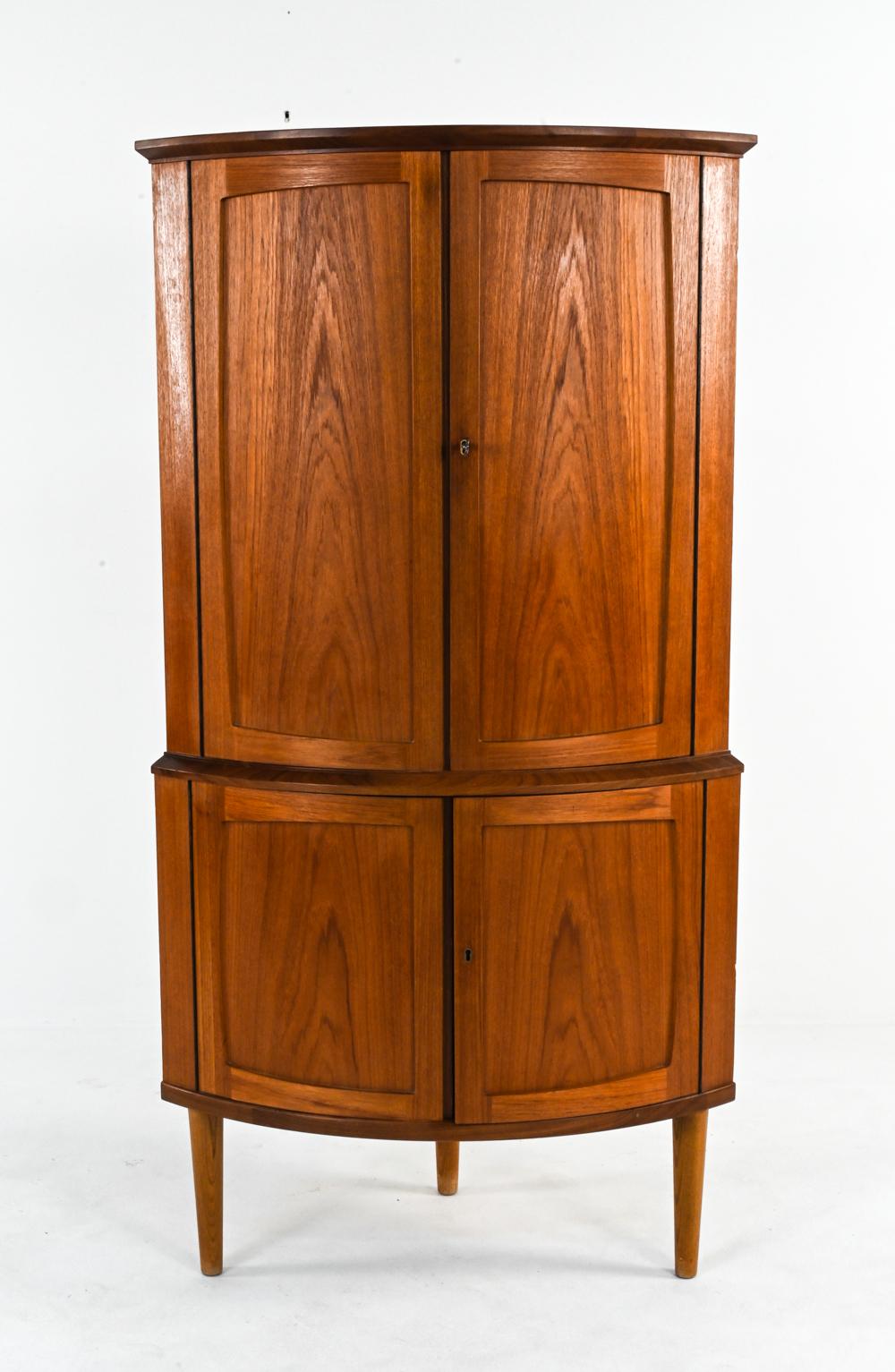 A beautiful Danish mid-century curved front corner cabinet in the manner of S. E. Peterson, c. 1960's. This finely crafted cabinet features quality teak book-matched veneer with an elegant flame-like grain and rich, warm coloration. On sturdy,