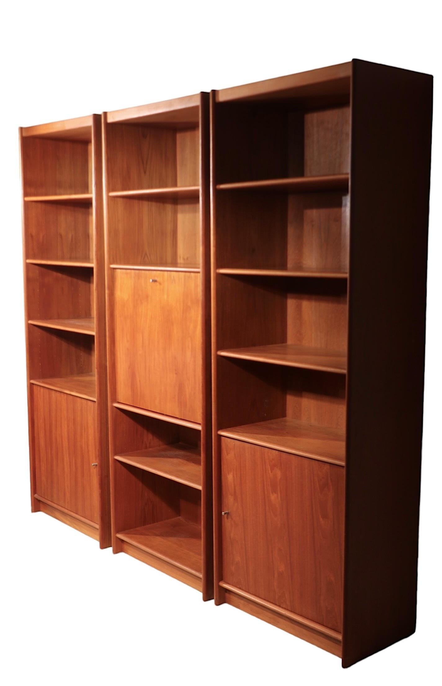 Exceptional freestanding wall unit, bookcase, fall front desk, constructed of teak, teak veneer, and aluminum. The set consists of three separate units, two with bookshelf tops over a one door cabinet, and the middle section, which has shelves above