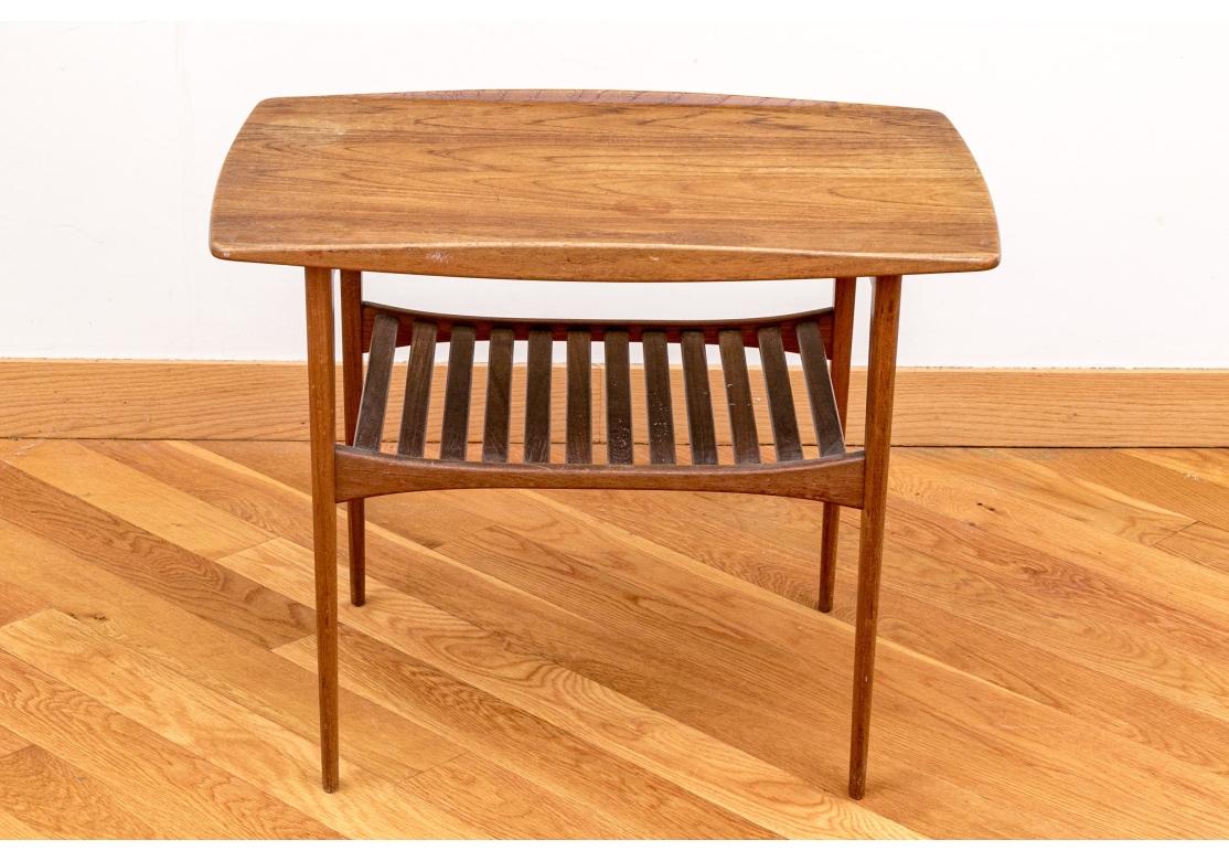 Classic Mid Century Danish design. Teak Side Table with fine form and having an Openwork magazine shelf below. 

Condition: Please see detail photos. Wear to finish with scratches and faded  water stains mentioned for accuracy as the presentation is