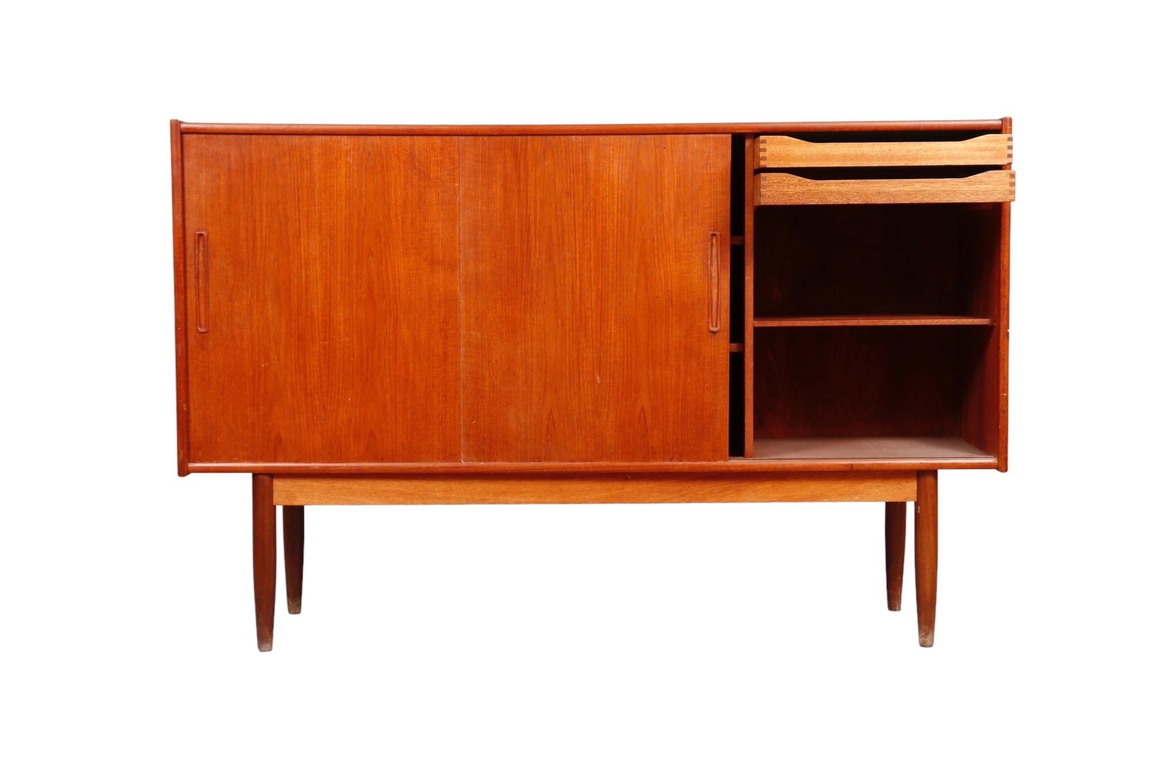 A Danish mid-century sideboard made of teak. Three cabinet doors slide with recessed handles to reveal adjustable shelves on the left and center. To the right are two felt lined dovetailed drawers. Round tapered legs are supported with a straight