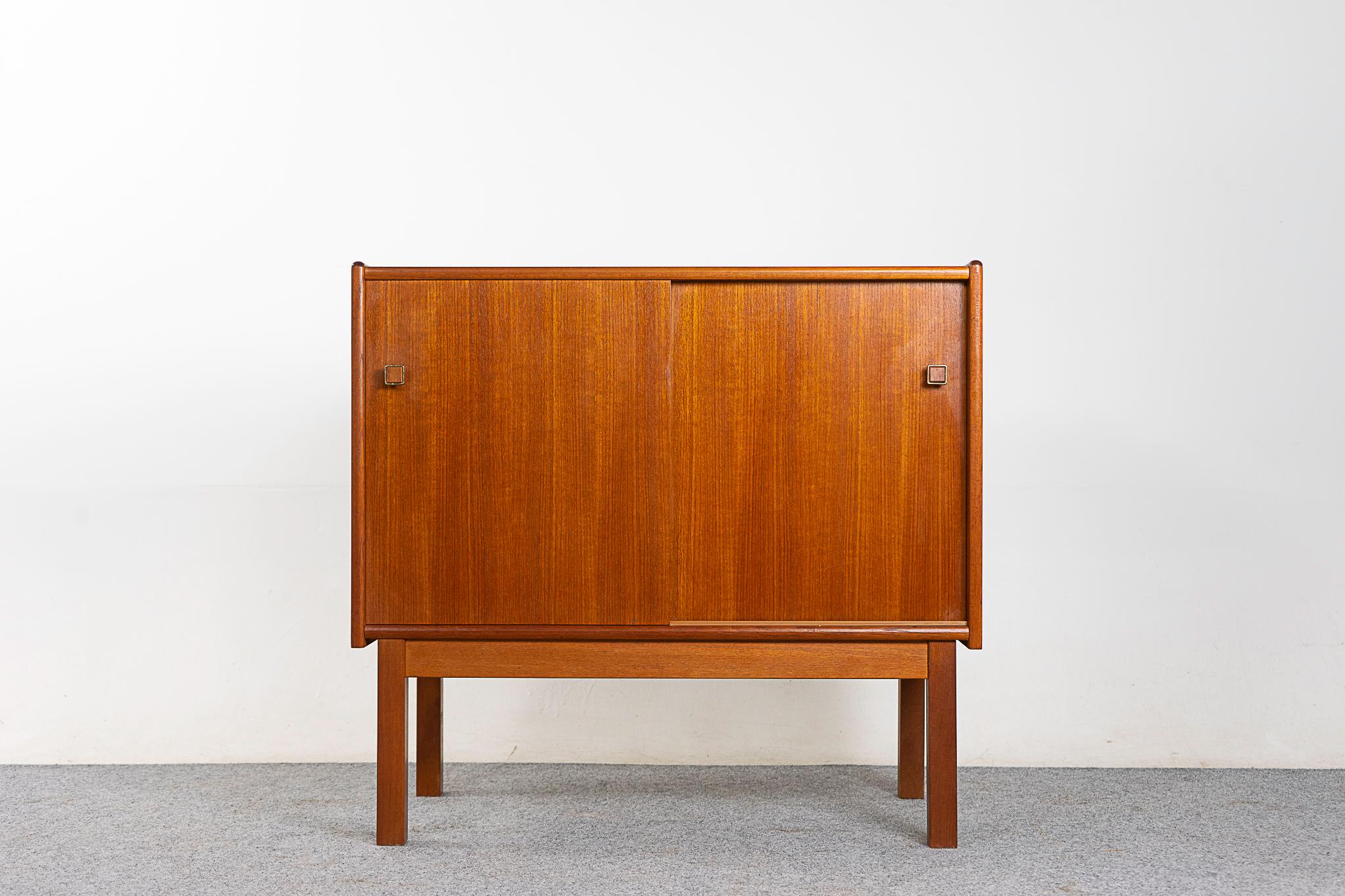 Teak Danish modern cabinet, circa 1960s. Low profile sliding door cabinet with interior shelf and darling pulls. Clean, simple lined design with lovely book-matched veneer. We have a matching pair, which would look 