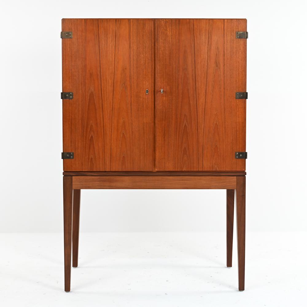 A handsome Danish mid-century teak highboy cabinet with a fitted interior featuring pull-out drawers/shelves with beautiful exposed dovetailed joints emphasizing the quality construction of this piece. This impressive chest sits on modern tapered