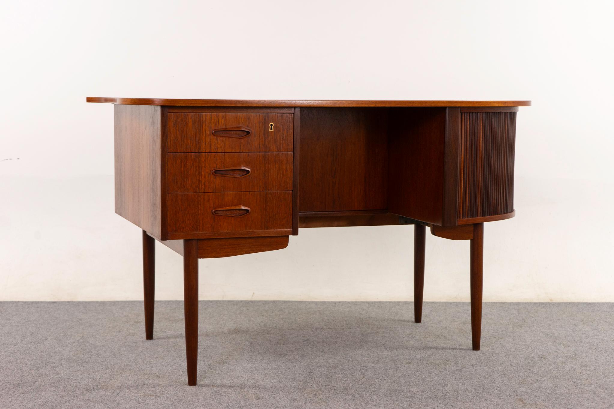 Teak Danish desk, circa 1960s. Unique asymmetrical desk with elegant tapering legs and darling atomic handles. Tambour door storage cubby with shelf, sleek dovetailed drawers, and backside open bookcase/display cubby. Finished on both sides, if