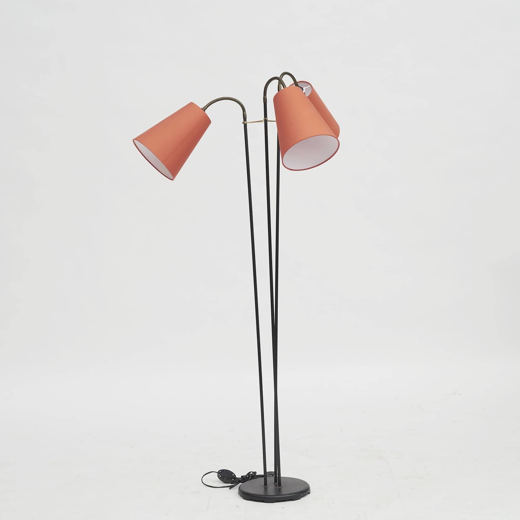 A Danish Mid-Century three-arm floor lamp with red / coral shades.
Black metal, arms coated with black fluted plastic material.

The three light points can be directed in different positions thanks to the three brass swivel arms.
Denmark