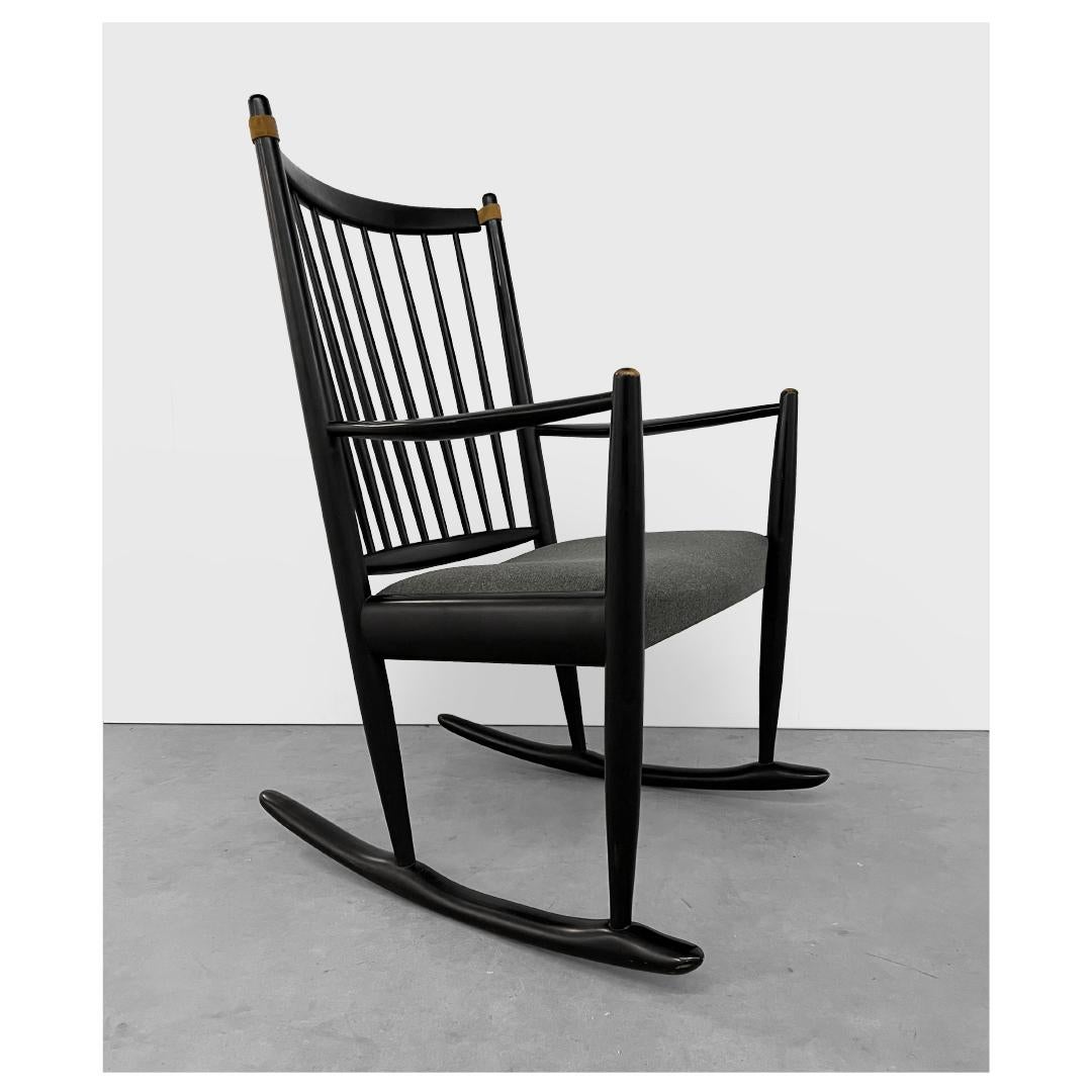 Danish midcentury rocking chair by Niels Eilersen, 1960s. It features a beautifully sculpted black lacquered solid beech frame with spindle back, unique leather top straps, new upholstery, wide seat and is extremely comfortable. In excellent