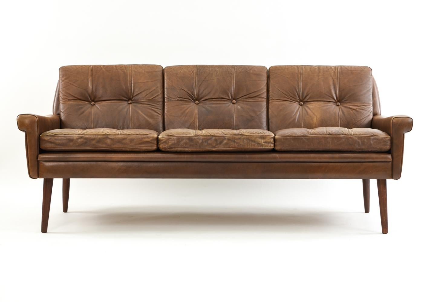 This Danish midcentury three-seat sofa designed by Svend Skipper and manufactured by Skippers Møbler is upholstered in supple, patinated brown leather with tufted backrests.