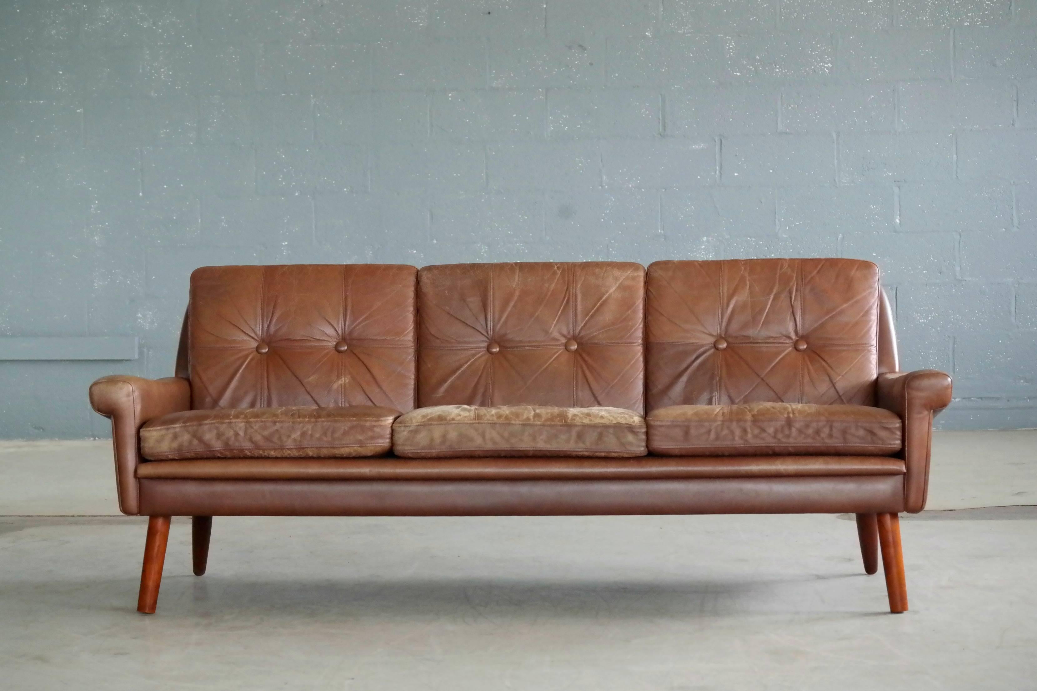 Classic Sven Skipper designed sofa in brown leather and tufted foam filled cushions raised on teak legs. The leather exhibits a nice well worn look including color fading and patina to the armrests as well as back and seat cushions and is perfect