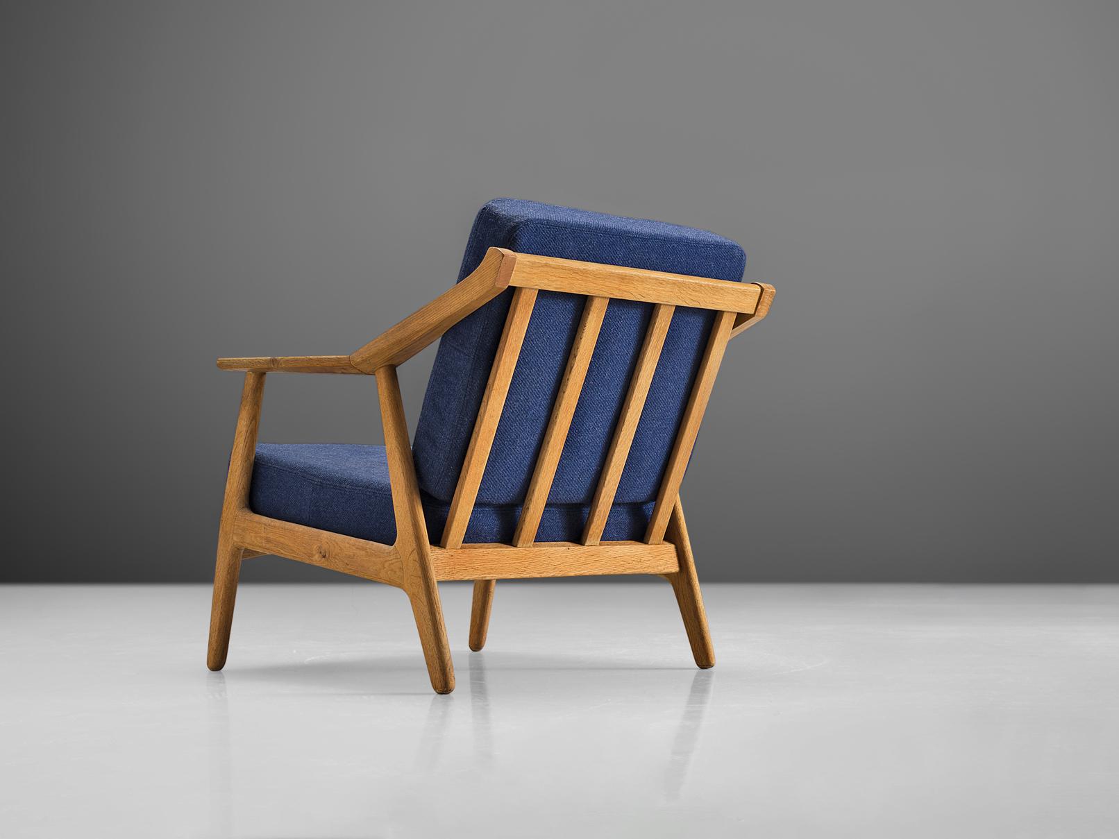Fauteuil, chêne, tissu bleu, Danemark, années 1960

Ce fauteuil sculptural est doté d'un dossier à lattes et de quatre pieds circulaires. Les accoudoirs sont exécutés avec un angle au milieu et c'est également à cet endroit que les pieds du dossier