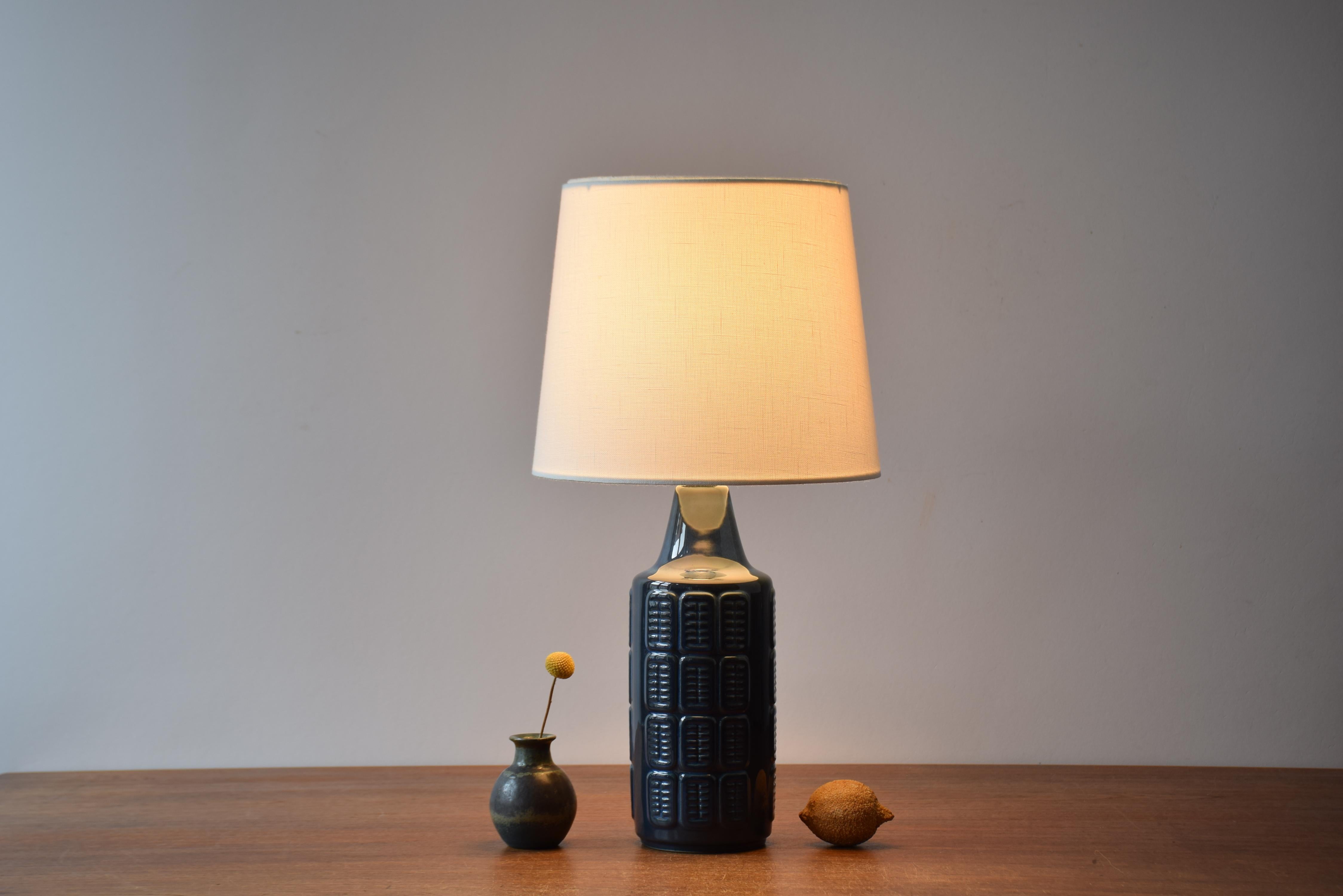 Table lamp by Einar Johansen for Søholm Stentøj, Denmark, circa 1960s.
The lamp has shiny blue glaze over an embossed repeated graphic decor. 

Included is a new lamp shade designed and made in Denmark. It is made of woven fabric with some texture