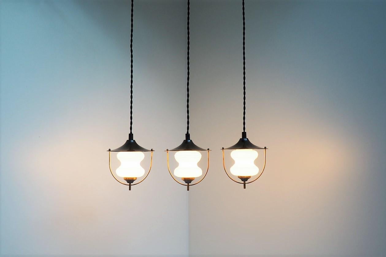 Set of three pendants made in white Opal glass together with a mix of brass and brownish lacquered metal shades. The pendants are manufactured in the 1940s by Lyfa.
The lovely shape of the glass combined with patinated brass and dark brown