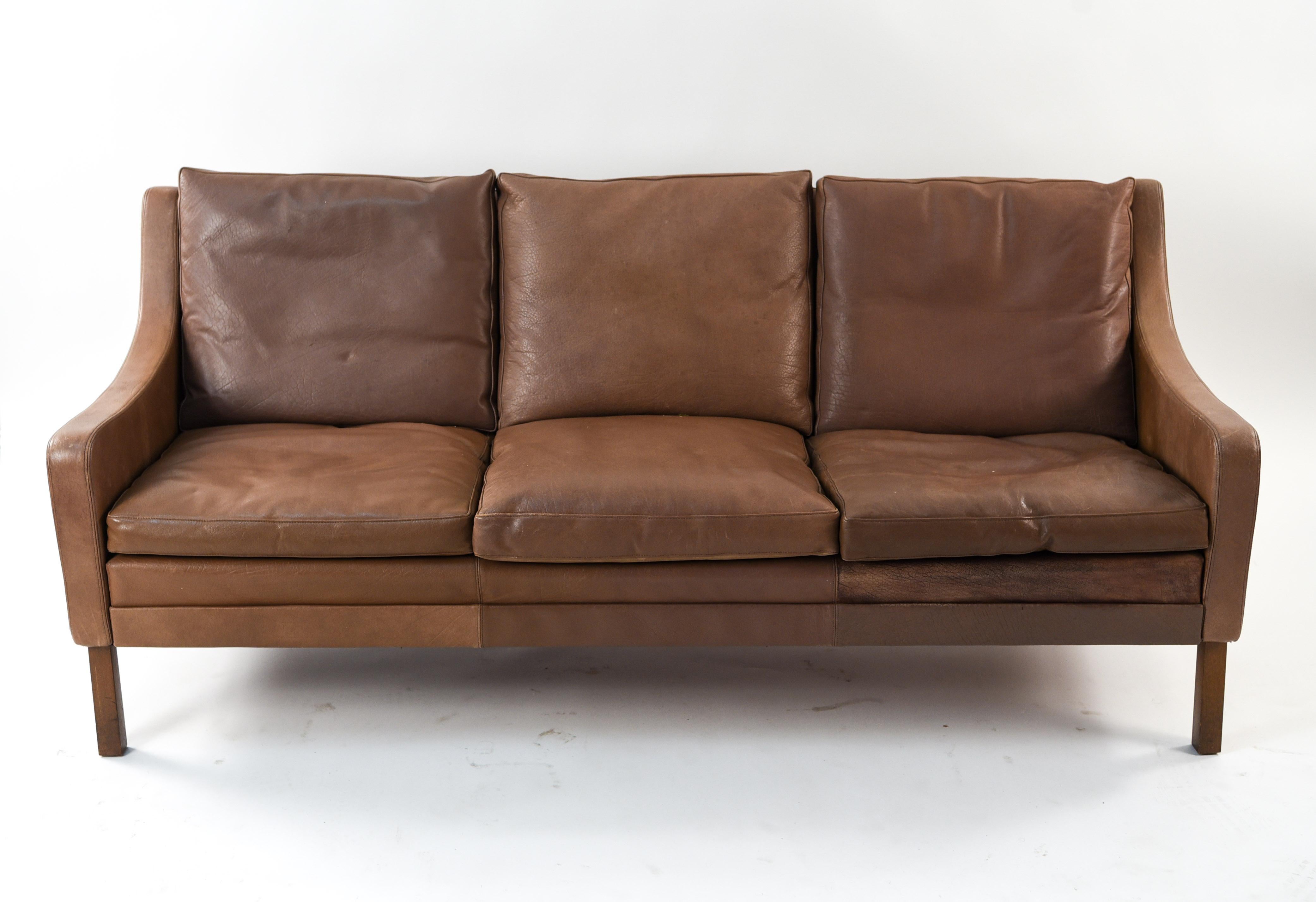 This Danish midcentury leather sofa is in the manner of designer Børge Mogensen. It seats three comfortably and is upholstered in vintage brown leather that has acquired a lovely patina from age and use.