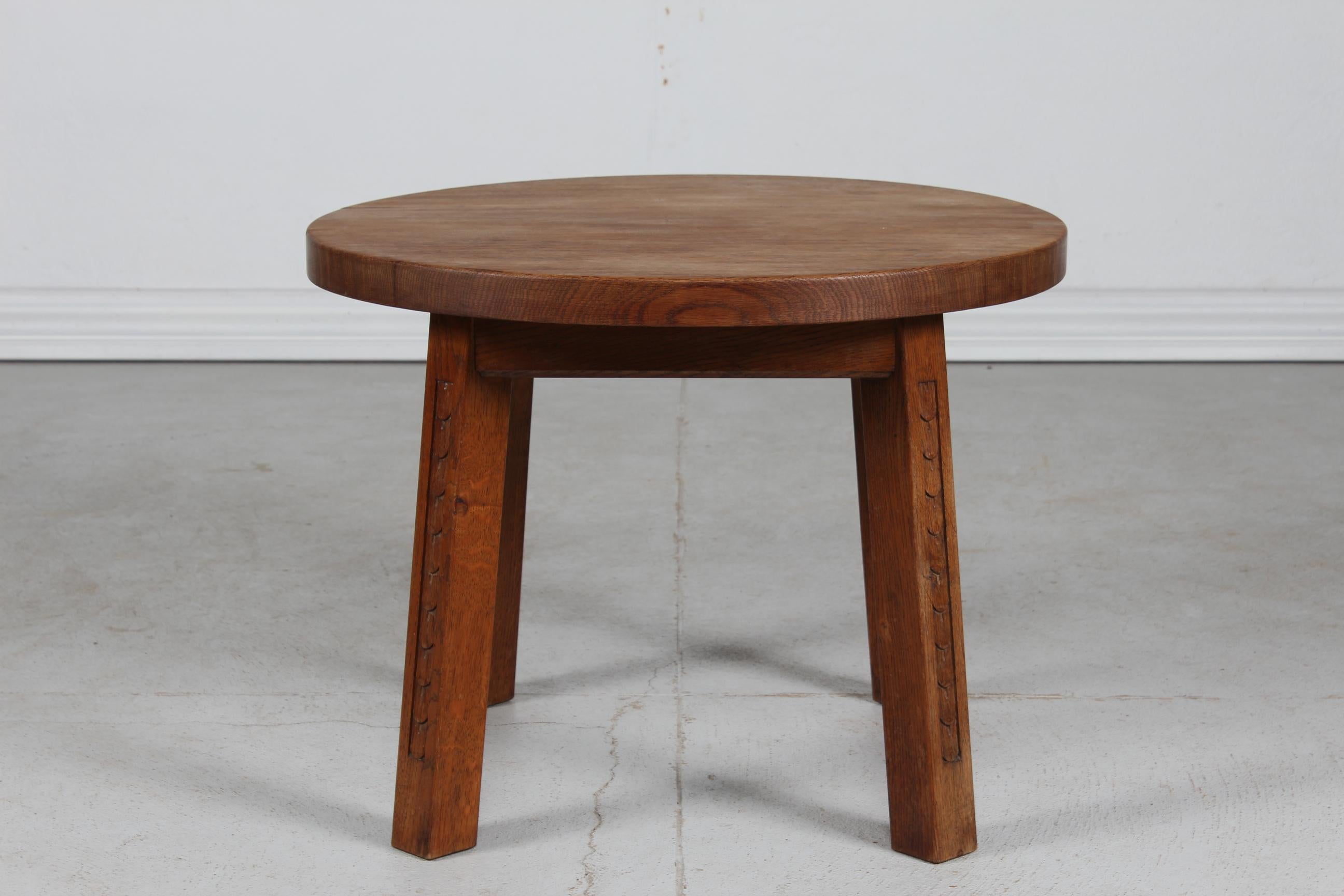 Danish brutalist style round coffee table of solid oak with a heavy tabletop on four square legs. On each of the four legs is a hand-carved relief.
Manufactured by a Danish cabinetmaker ca. 1950s. 
The design is in the style of Otto Færge and Axel