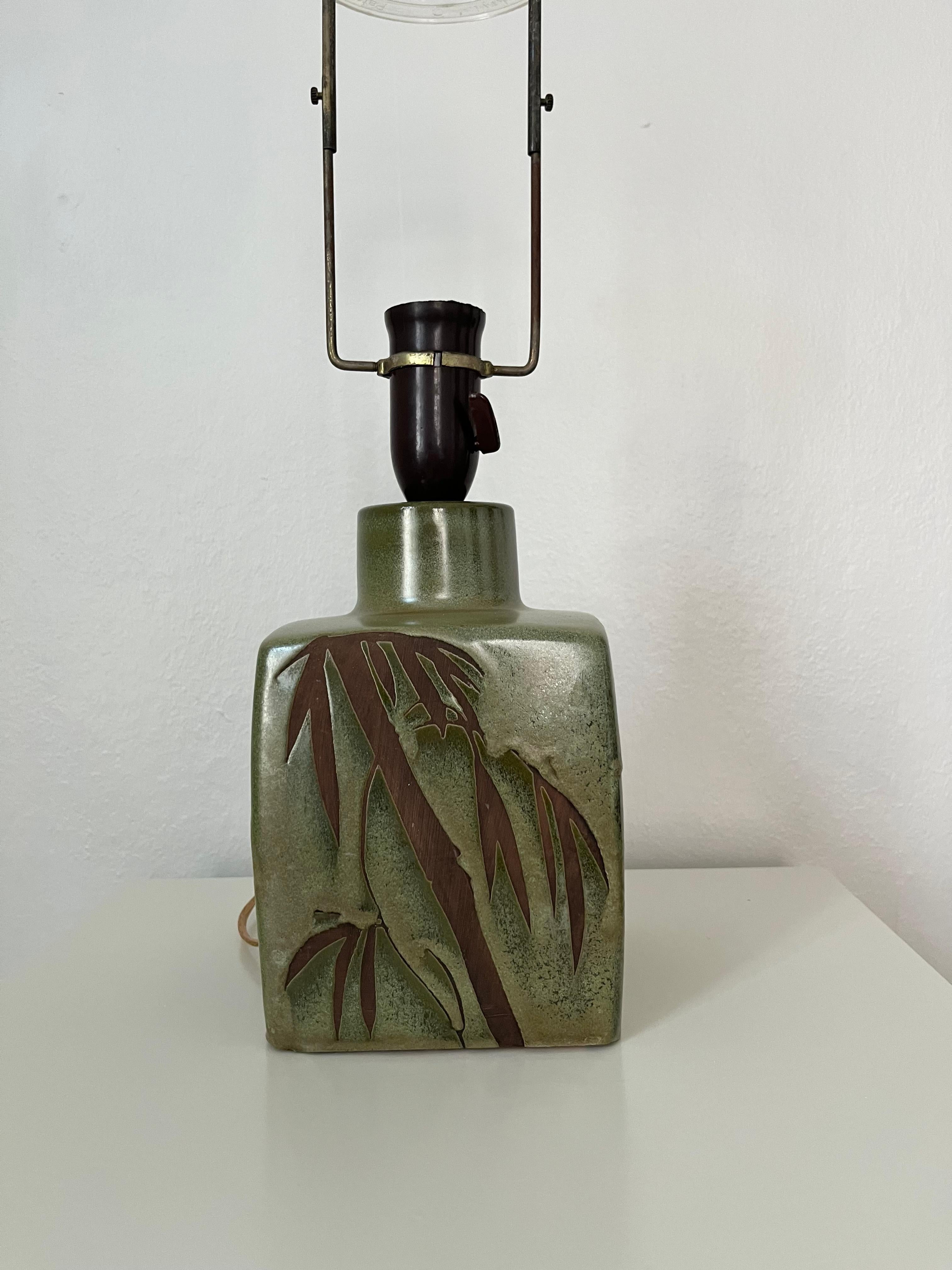 Danish midcentury ceramic table lamp with palm decorations

Danish midcentury ceramic table lamp in a square shape with palm decorations on all sides. Faded green and brown tones. European wired with sucket for E-27 light bulb and is working fine,