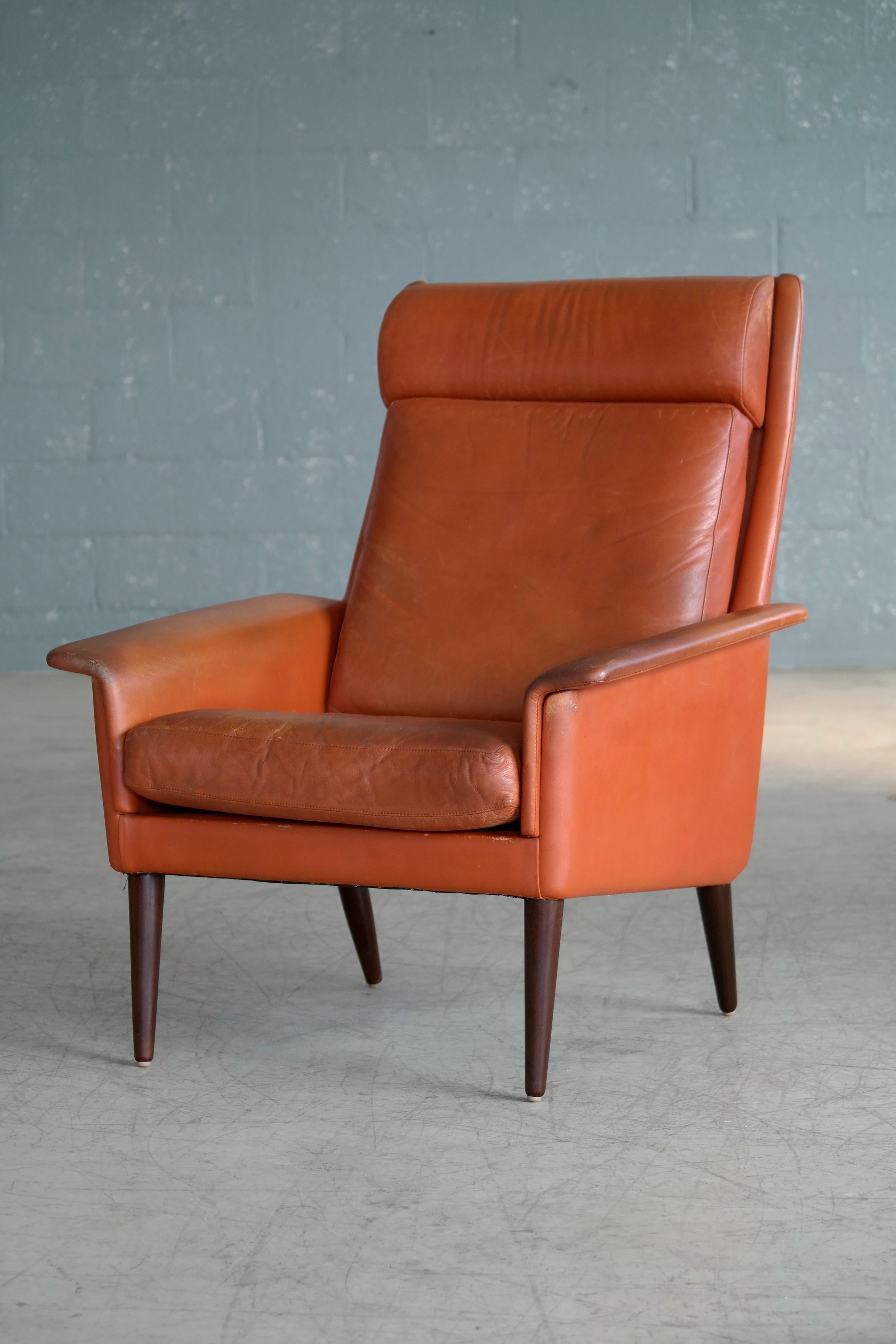 Sleek and very cool Danish 1960s cognac colored high back lounge chair carrying the makers label of Sibast furniture on the bottom frame. The chairs is very much in the style of Arne Vodder who did design for Sibast and it's very similar to design
