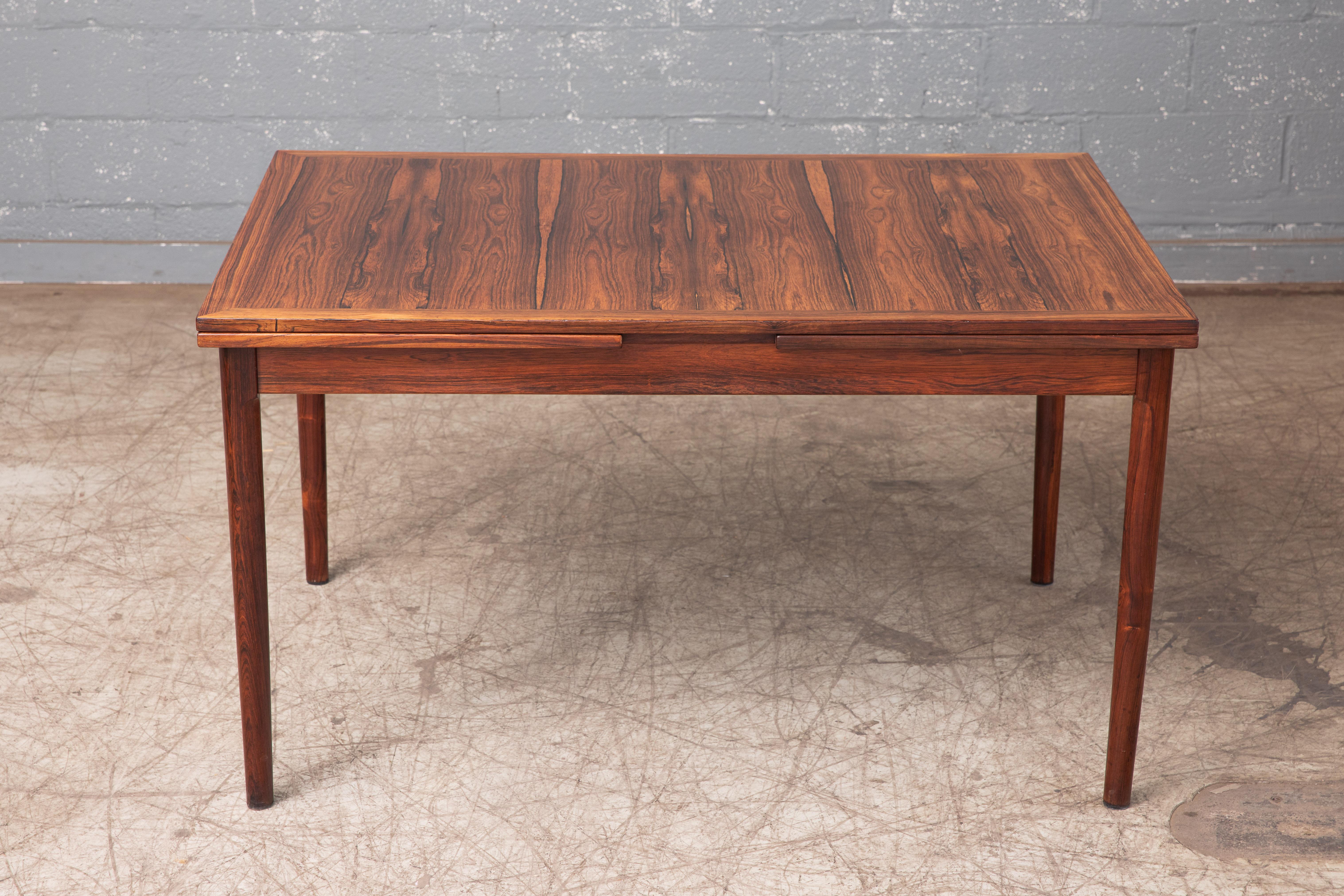 A stunning Danish midcentury rosewood draw leaf dining table made in Denmark in the 1960s. Features beautiful rosewood grain with solid thick edges and sculpted legs. Expandable with two draw leaves to comfortably seat up to ten people for dinner.