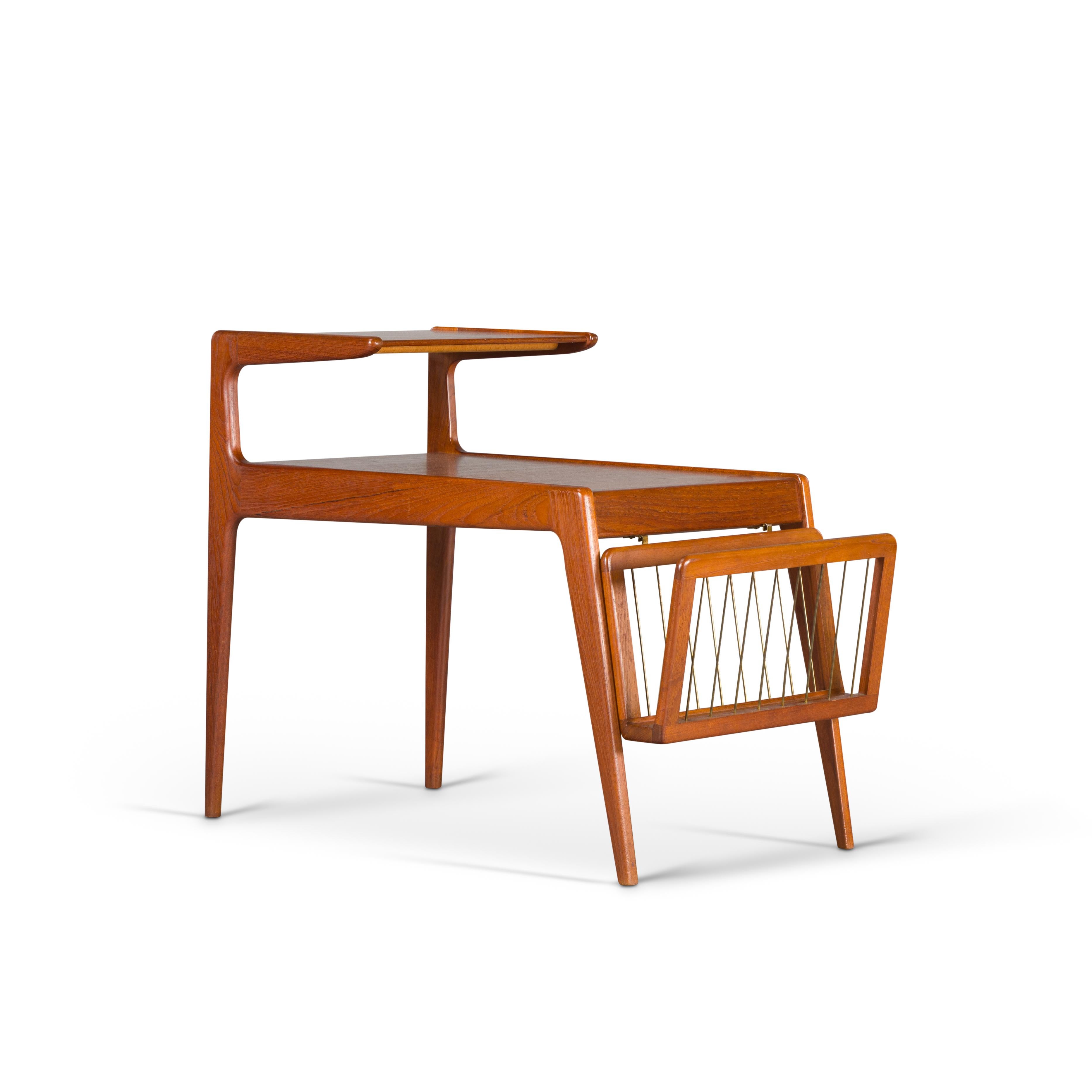 Danish teak side table with removable magazine rack designed by Kurt Ostervig for Jason Møbler. The design encompasses a top tier a lower tier and a magazine rack. The magazine rack can easily hold 10 magazines or newspapers and hooks into a set of