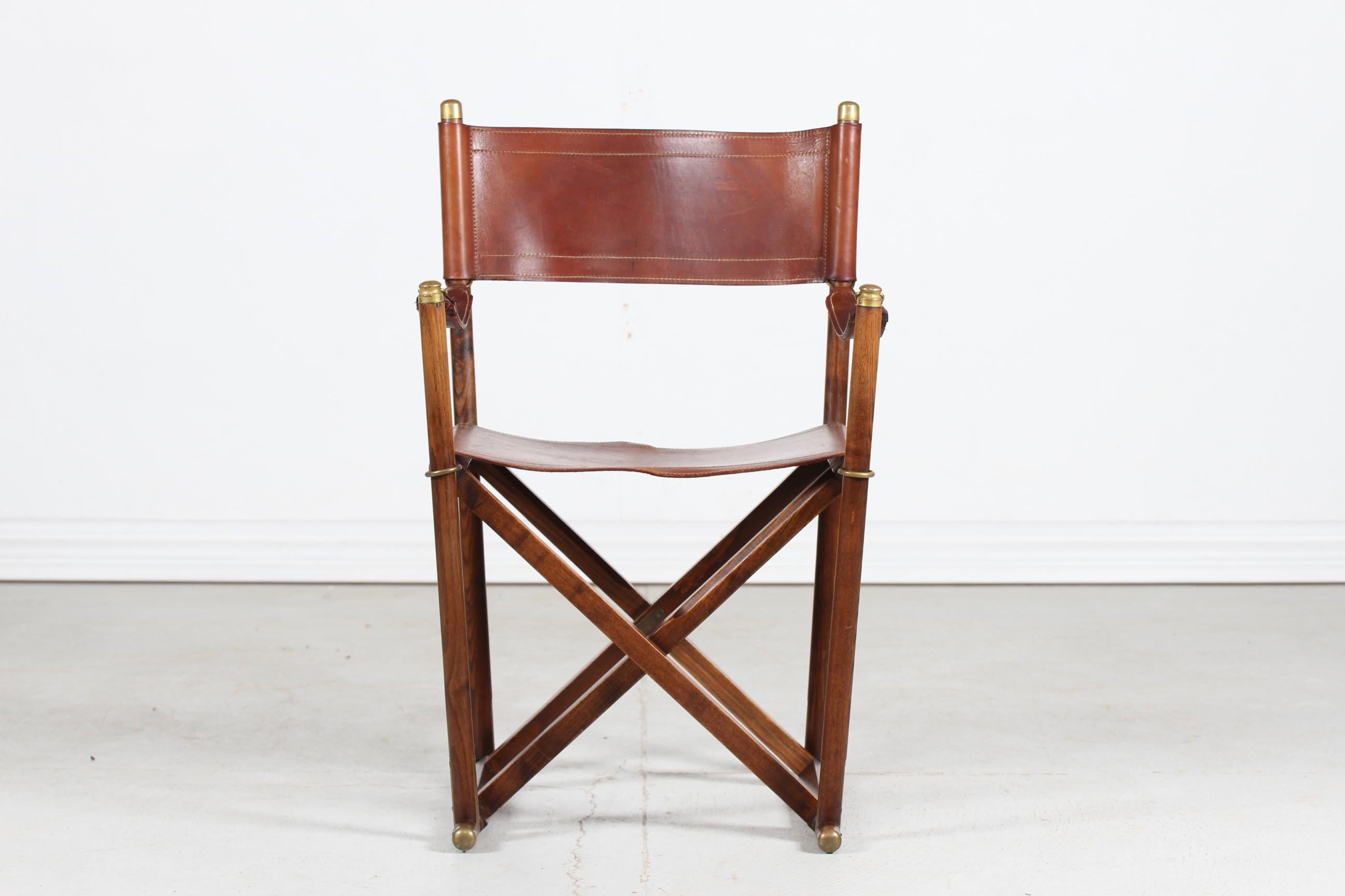 Danish midcentury directors chair with frame made of dark wood (most likely elm) mounted with high quality brass fittings. The seat, backrest and armrests are made of core leather with beautiful patina.

The designer of this chair is unknown but