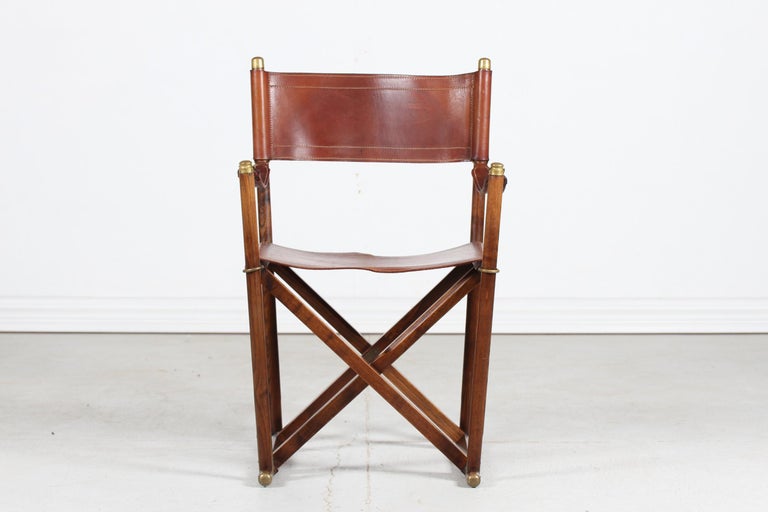 Danish midcentury directors chair with frame made of dark wood (most likely elm) mounted with high quality brass fittings. The seat, backrest and armrests are made of core leather with beautiful patina.

The designer of this chair is unknown but