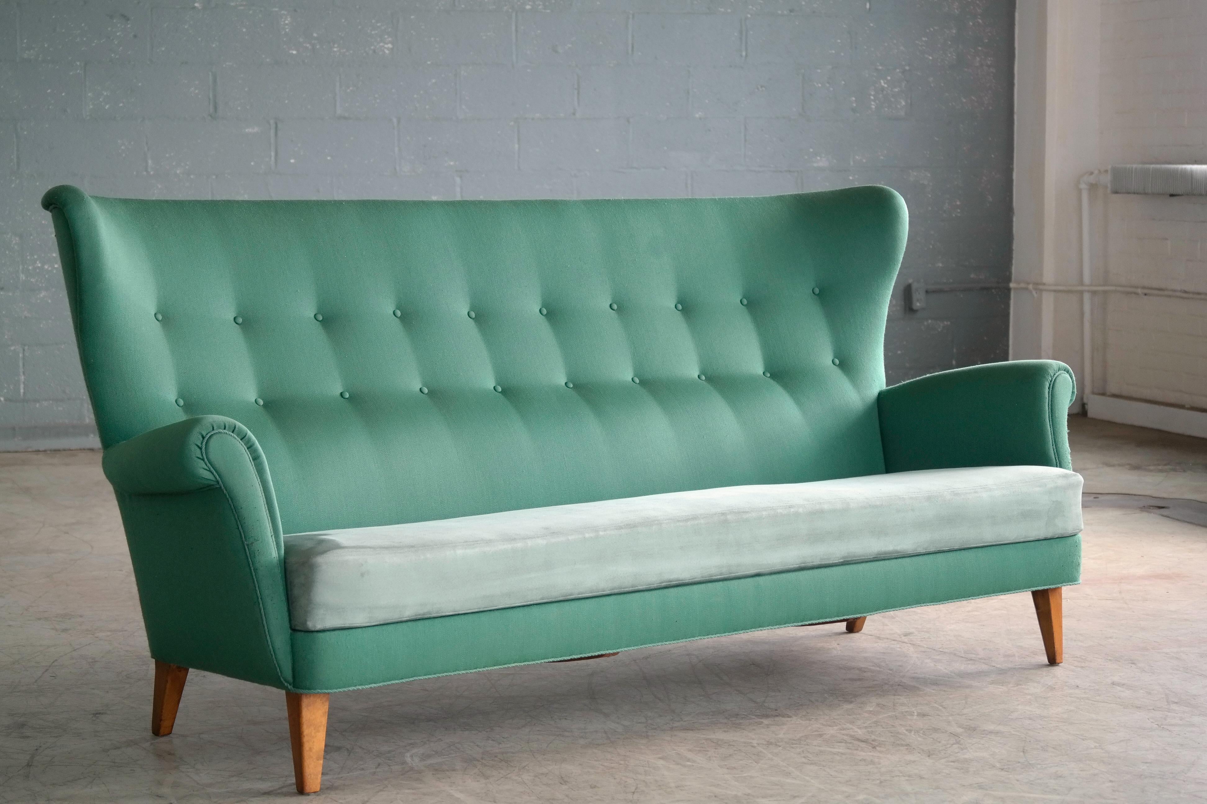 Very charming high back or wingback 1950s sofa from Denmark. The sofa is very reminiscent of Fritz Hansen's model 8112 loveseat but in this case somewhat larger and with a loose seat cushion covered in ultra suede and we are unsure of who the