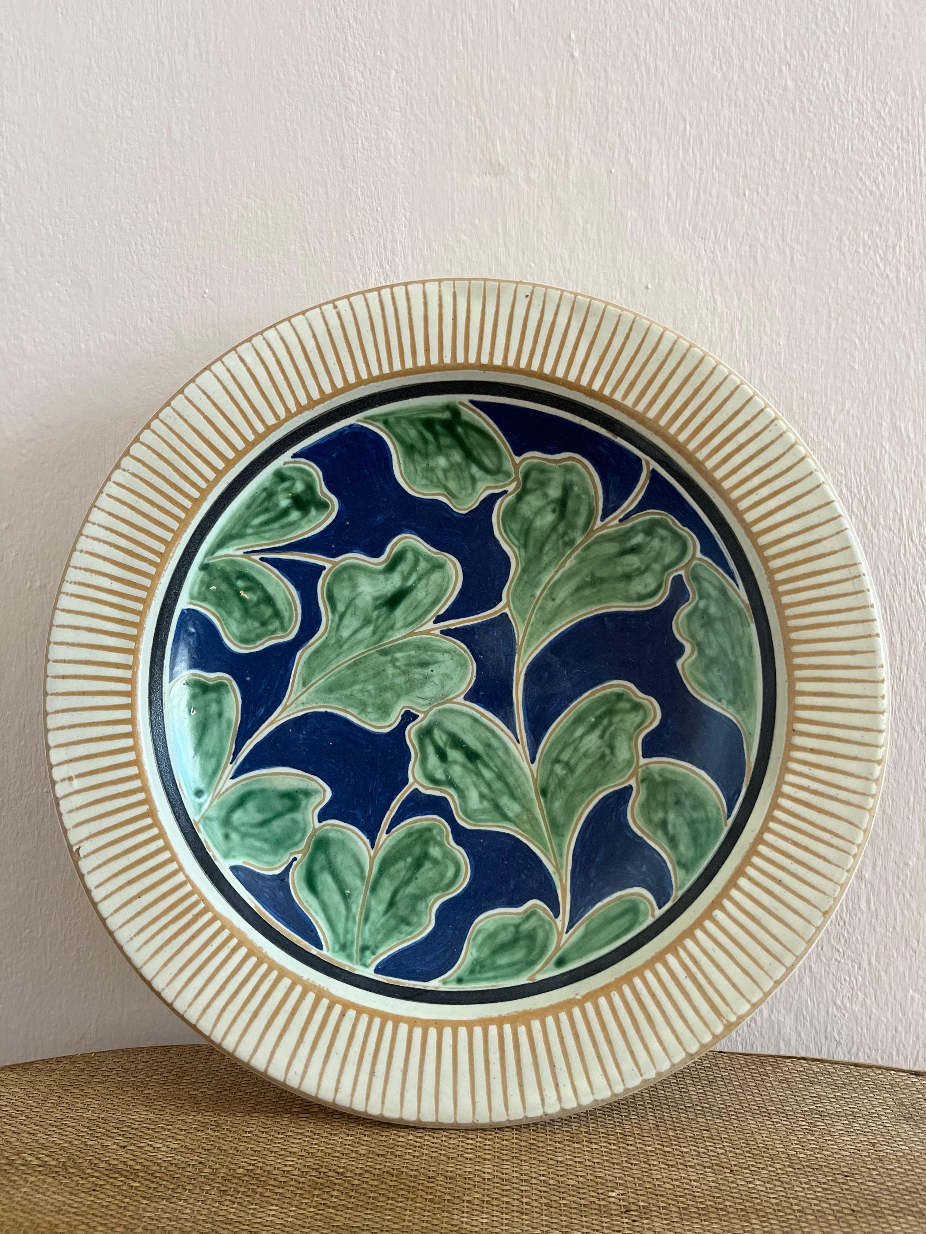 Very decorative Danish midcentury ceramic dish with incised lines and glazed in cream, green and blue nuances with leaf decorations. Indistinct signature, very much in the style of Danish pottery Haunsø Ceramics. 
The piece is in overall good