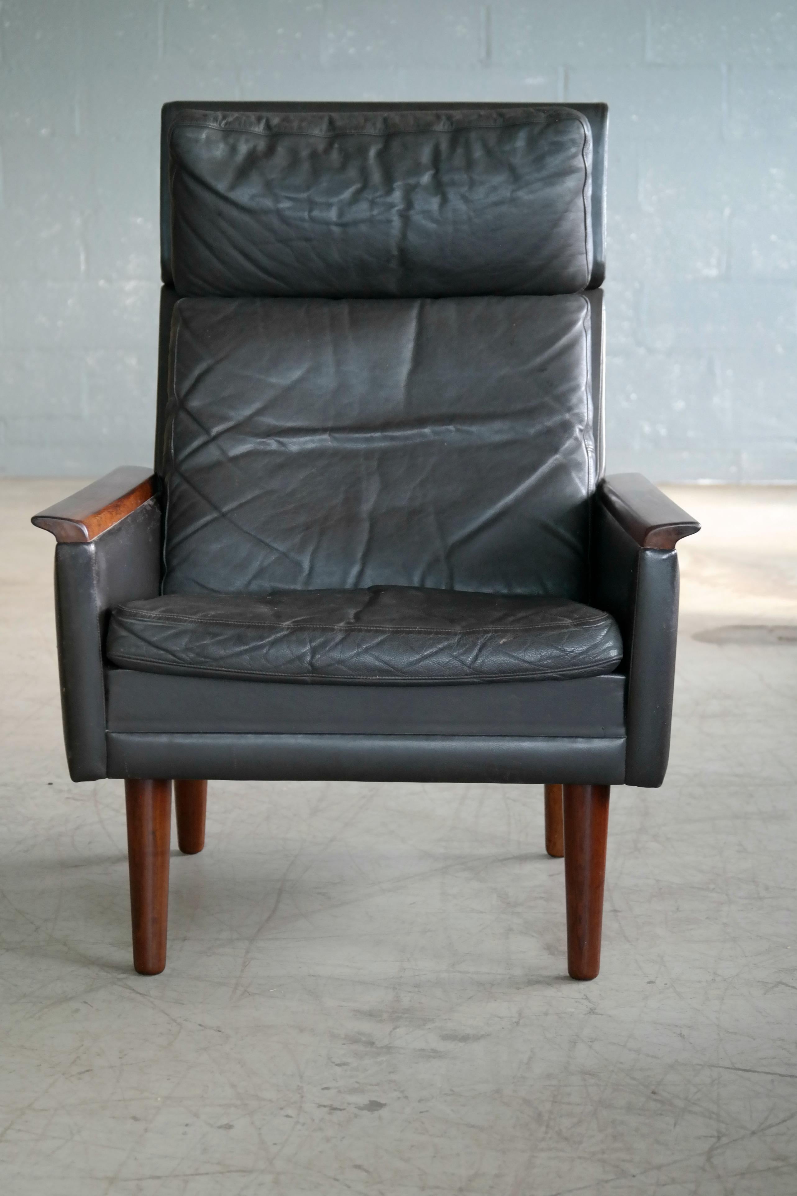Beautiful very elegant high back lounge chair in dark almost black cordovan colored leather with semi-down filled cushions. Armrests in solid rosewood with beautiful grain and color. The chair design bear some resemblance to Knut Saeter's upscale