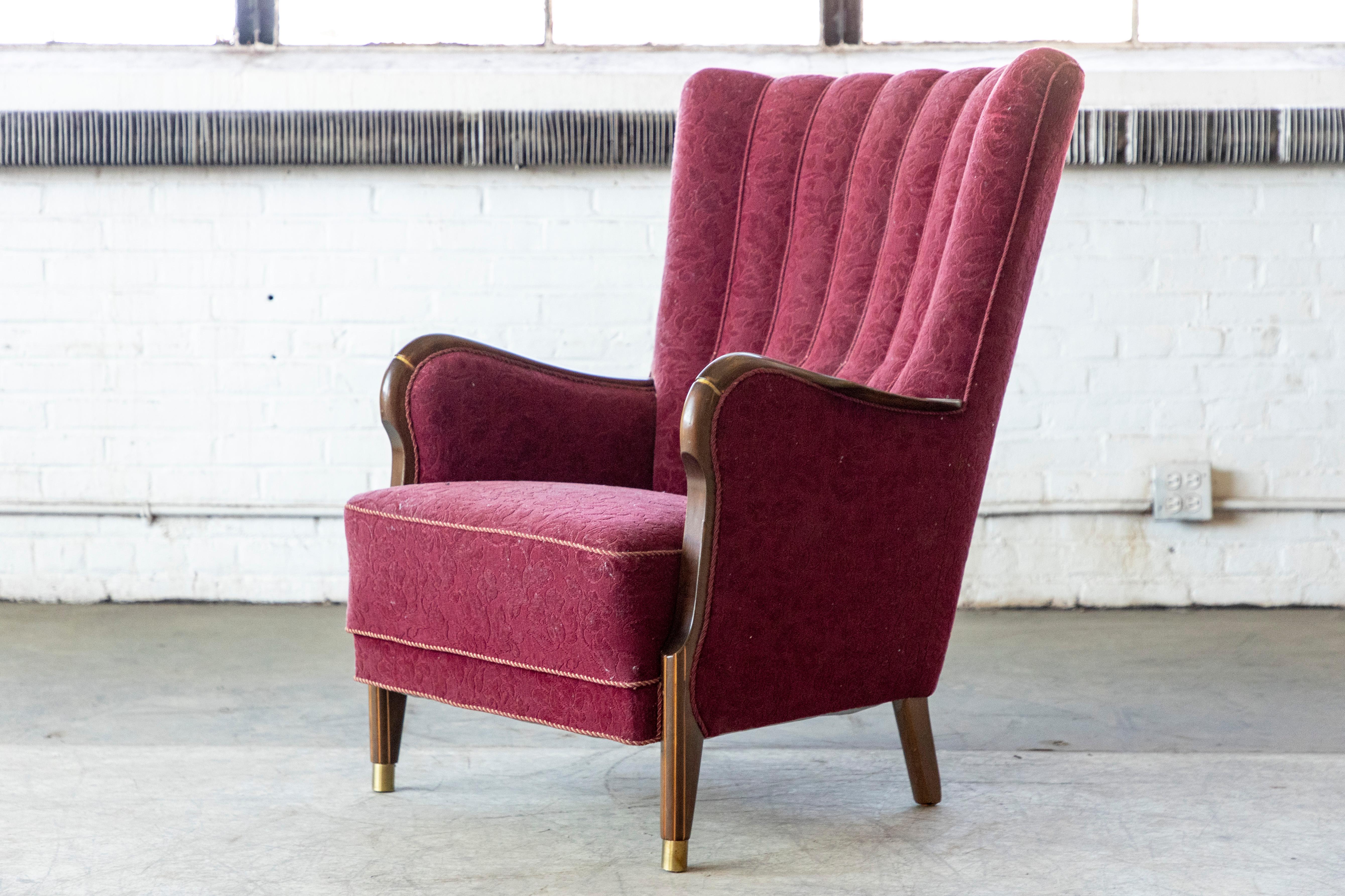 A rare find. Danish midcentury chair from the late 1940's or early 1950s. The wooden frame on the armrests and the tapered thin front legs capped with brass shoes is reminiscent of Frits Henningsen's designs. Made from mahogany upholstered in a dark