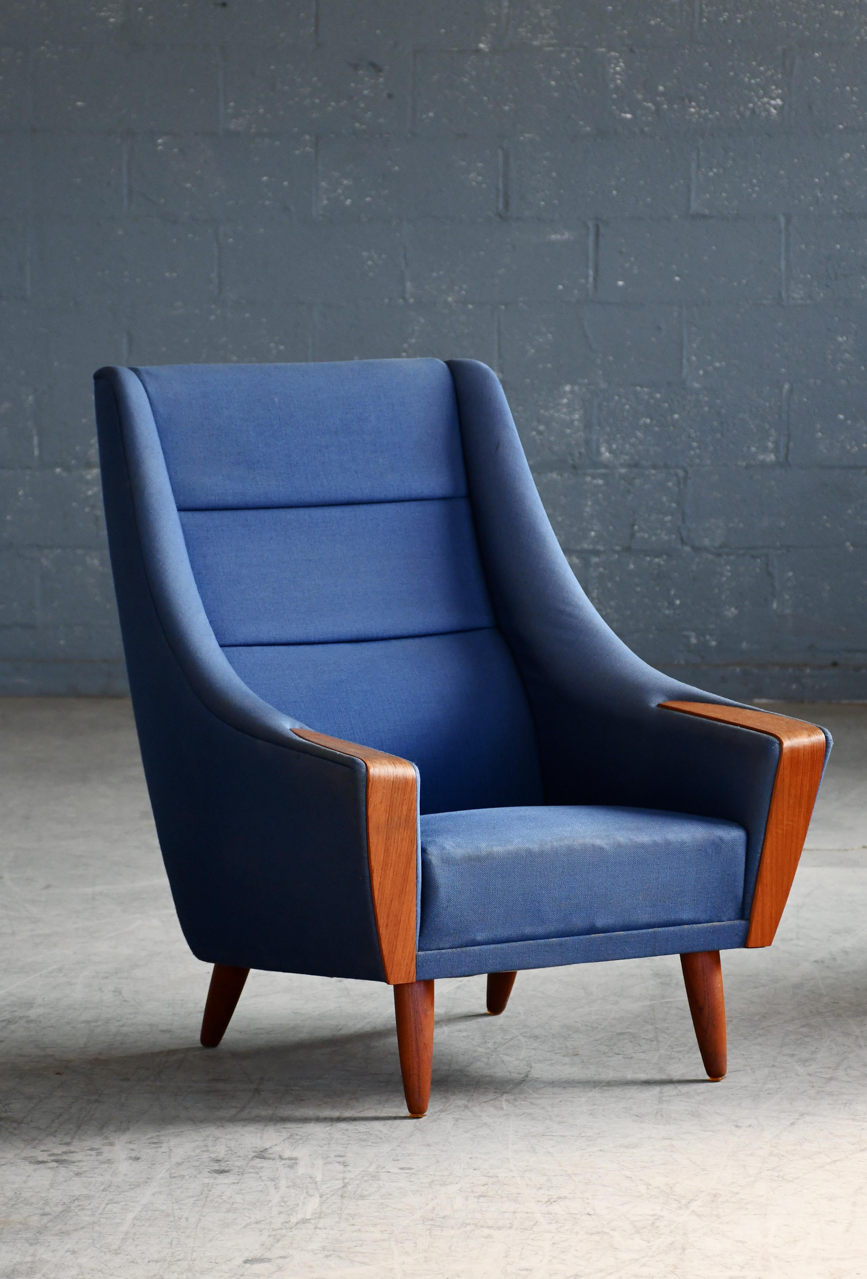 Genial tumbona danesa de mediados de siglo con respaldo alto, patas de teca y detalles de teca en los reposabrazos.  Epitomiza el estilo de alrededor de 1960. Esta silla es muy del estilo de Kurt Ostervig para Rolschau Mobler, pero no estamos