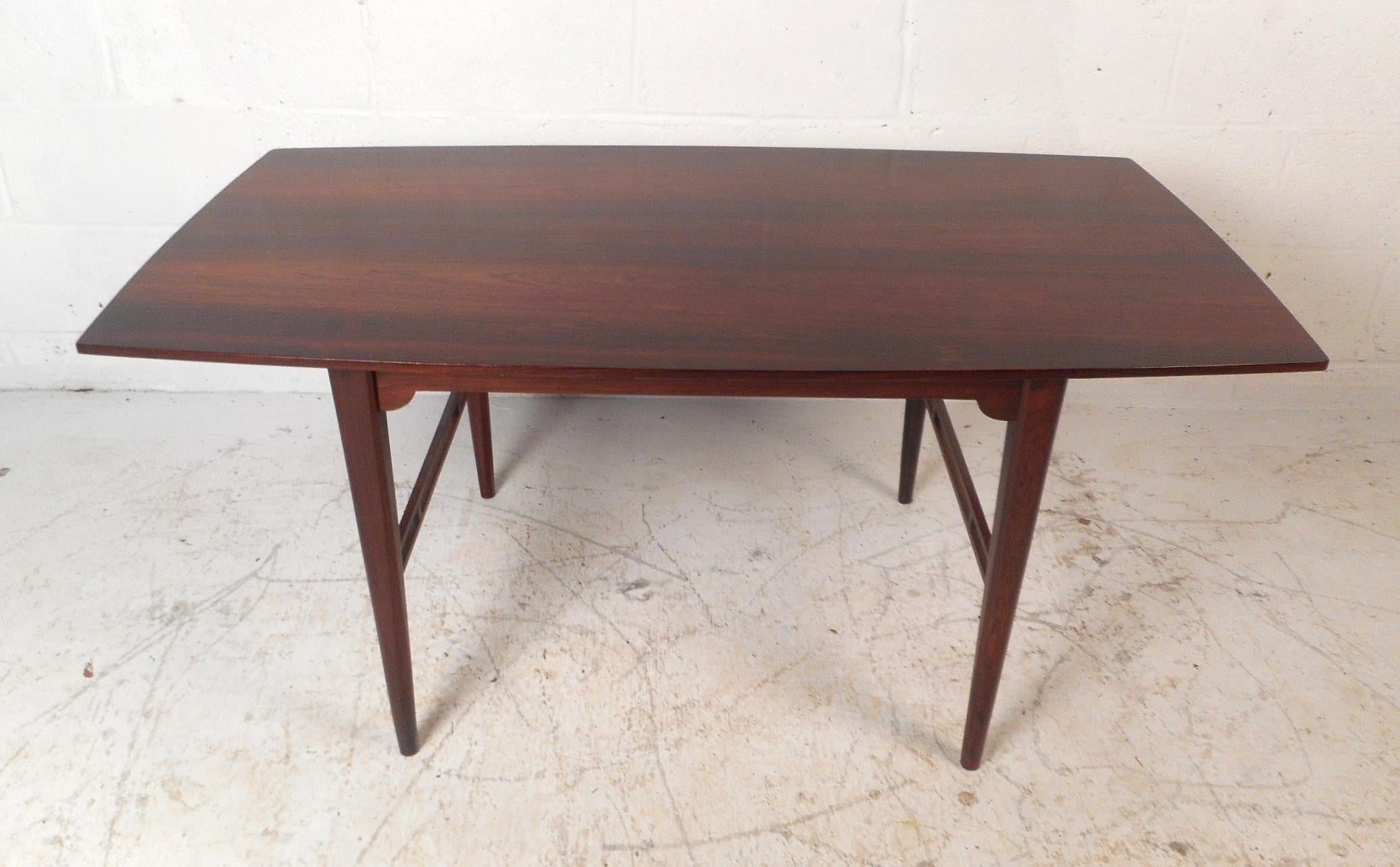 A beautiful vintage modern coffee table with uniquely shaped tapered legs and elegant rosewood wood grain. This Sleek Danish modern coffee table features an unusually shaped top and sculpted stretchers on each side. This wonderful coffee table makes